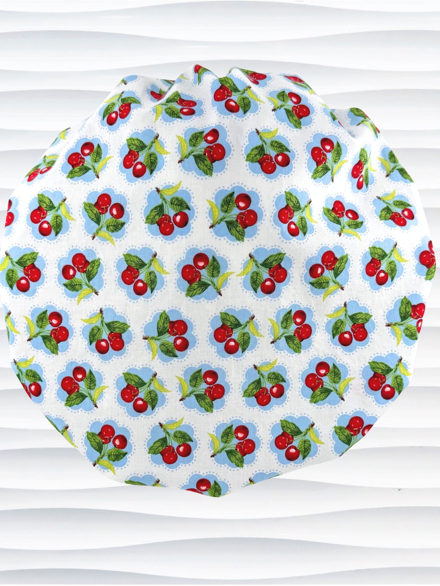 Bouffant style surgical scrub cap by JensCaps with red cherries and blue polka dots on white cotton fabric and displayed on a mannequin head.