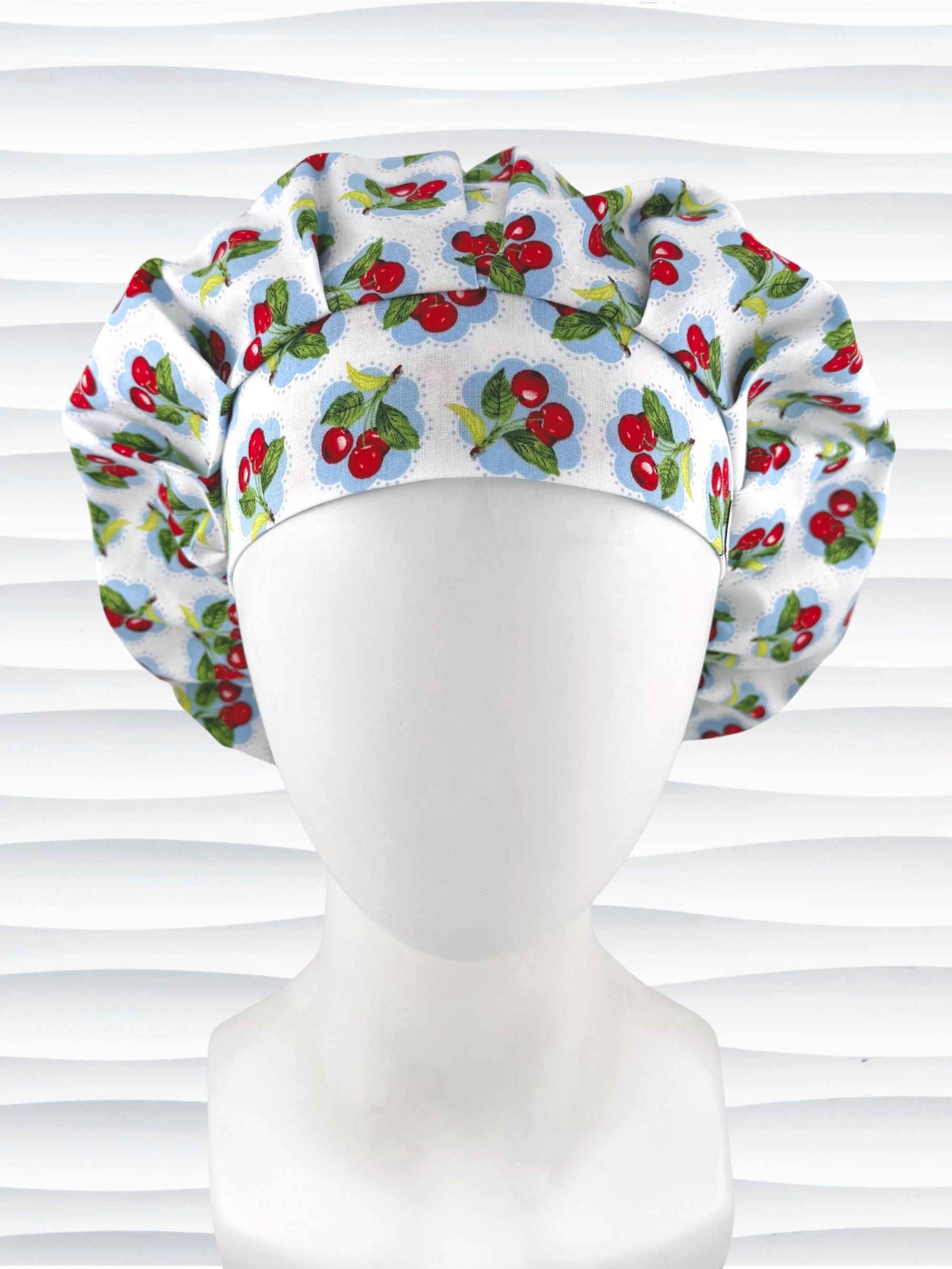Bouffant style surgical scrub cap by JensCaps with red cherries and blue polka dots on white cotton fabric and displayed on a mannequin head.