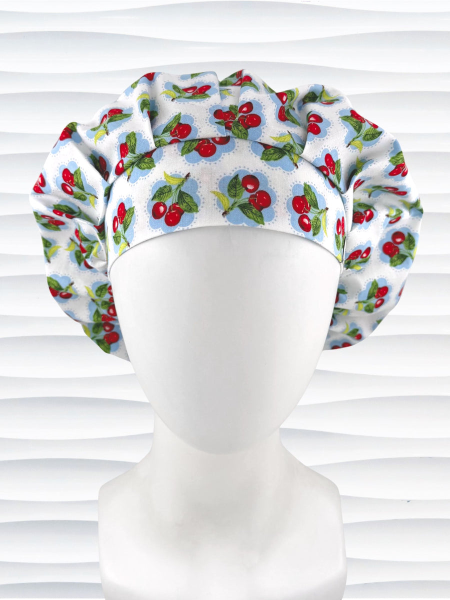 Bouffant style surgical scrub cap by JensCaps with red cherries and blue polka dots on white cotton fabric and displayed on a mannequin head.