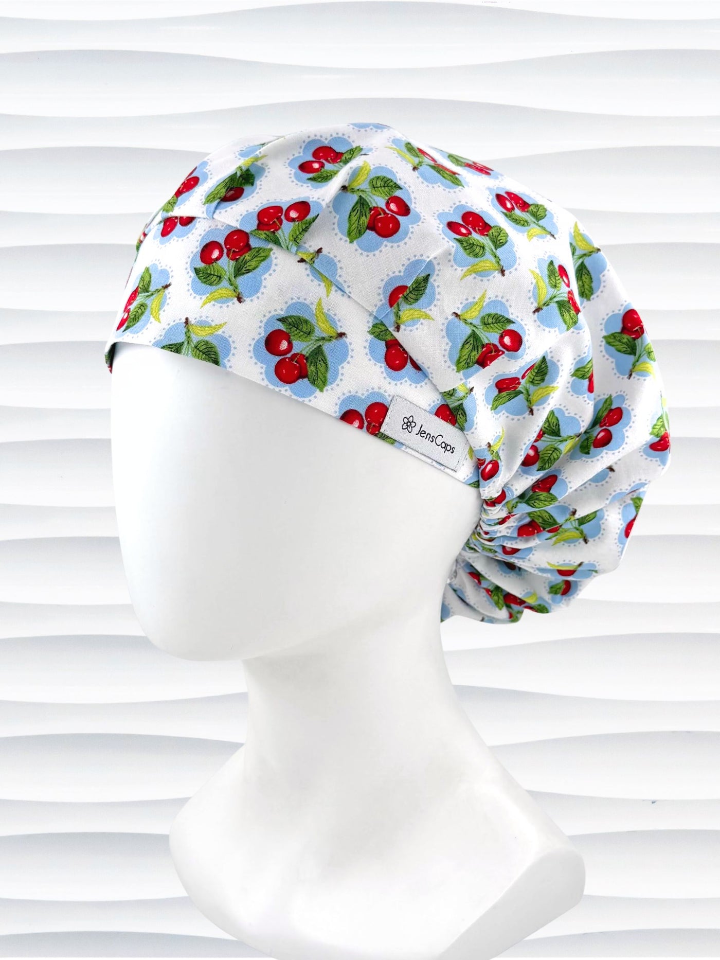 Bouffant style surgical scrub cap by JensCaps with red cherries and blue polka dots on white cotton fabric and displayed on a mannequin head.