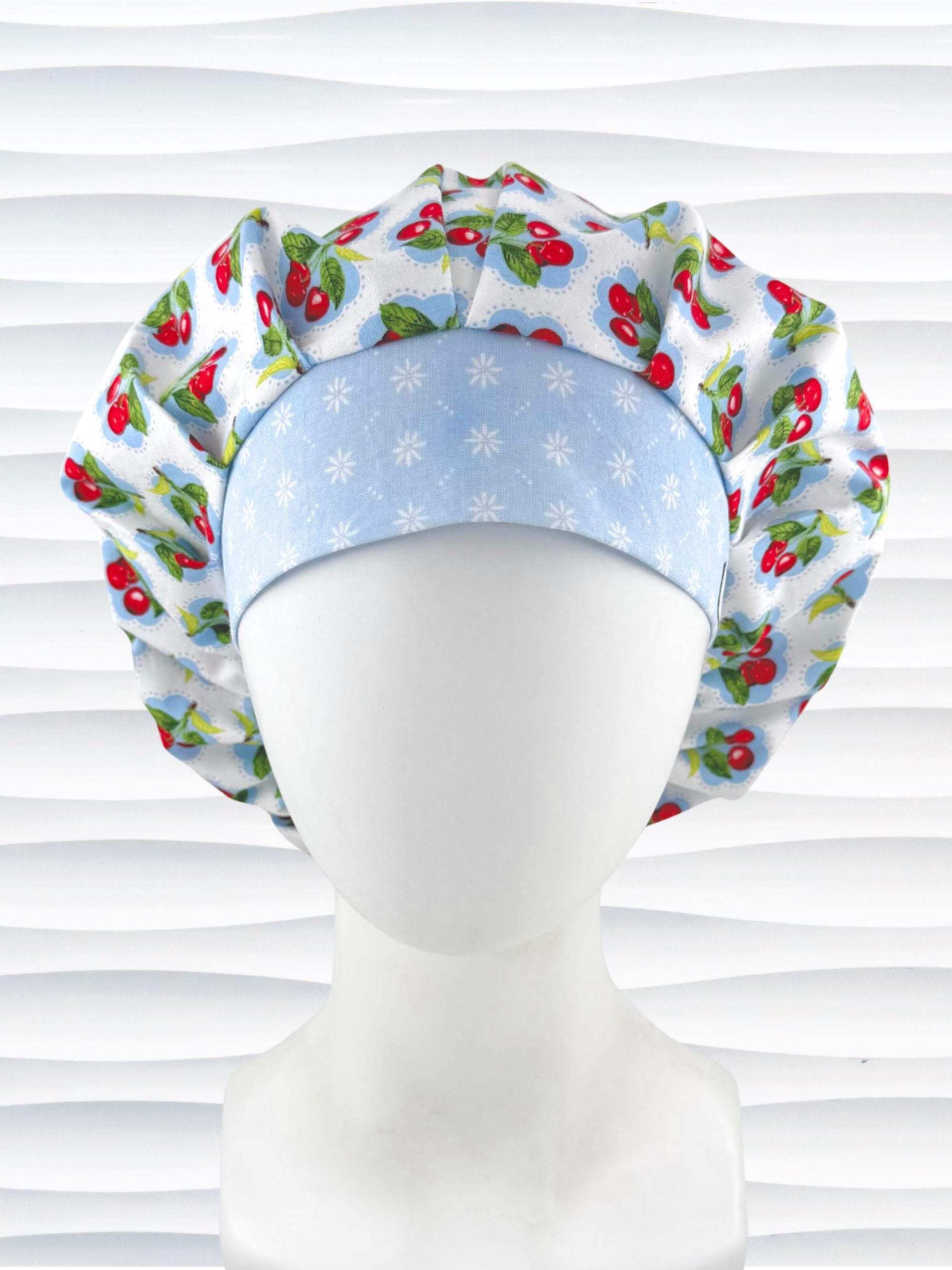Bouffant style surgical scrub cap by JensCaps with red cherries and blue polka dots on white cotton fabric and displayed on a mannequin head.