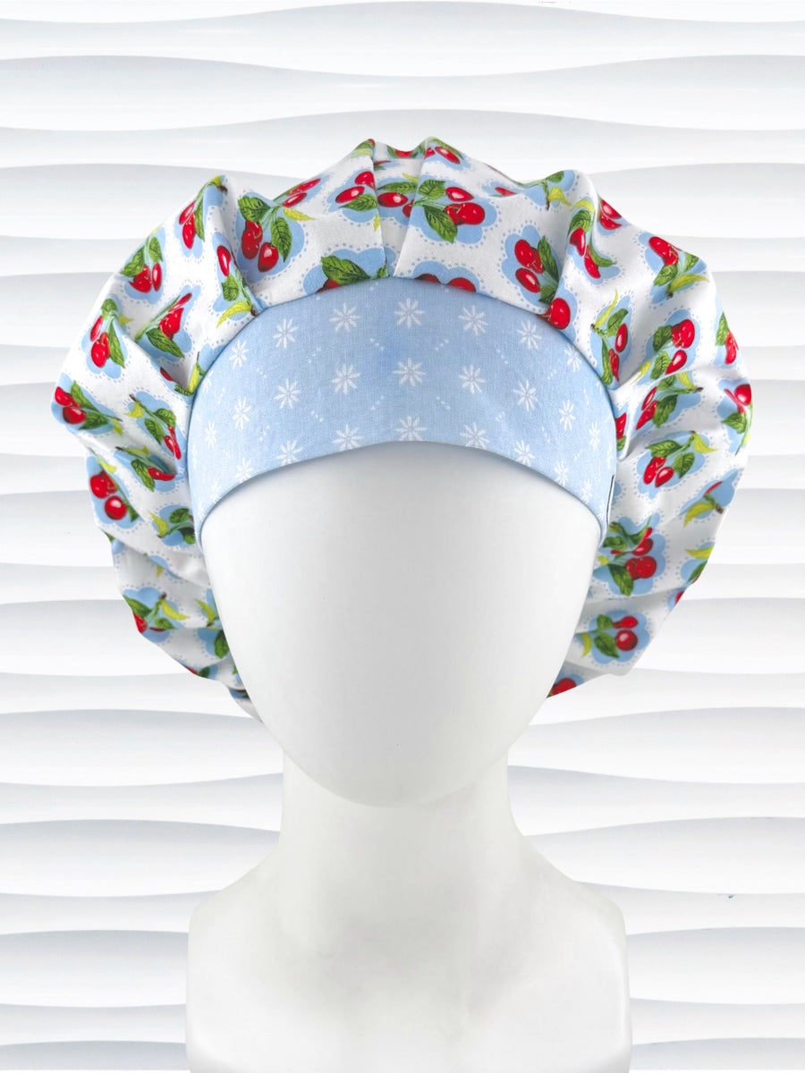 Bouffant style surgical scrub cap by JensCaps with red cherries and blue polka dots on white cotton fabric and displayed on a mannequin head.