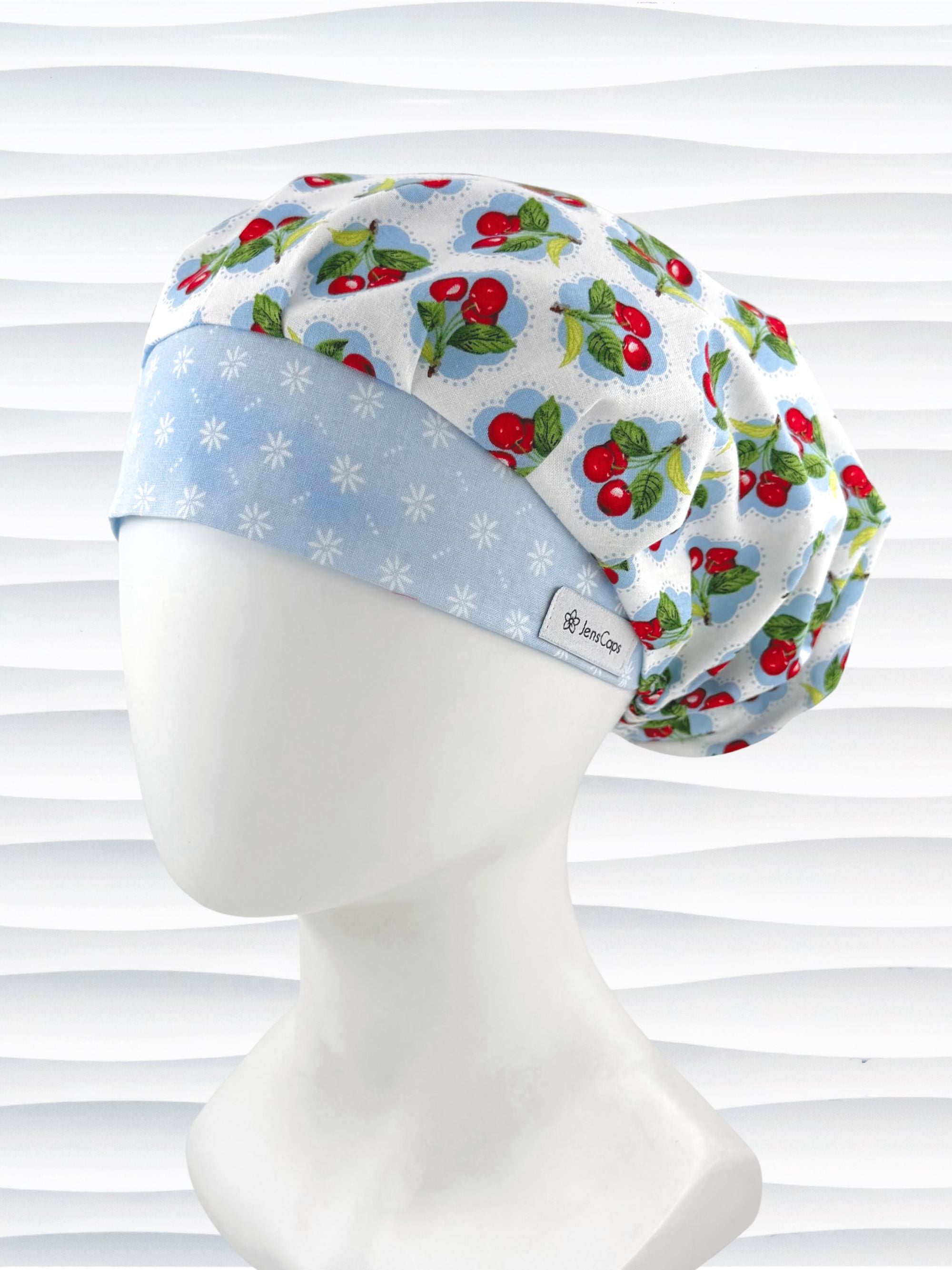 Bouffant style surgical scrub cap by JensCaps with red cherries and blue polka dots on white cotton fabric and displayed on a mannequin head.