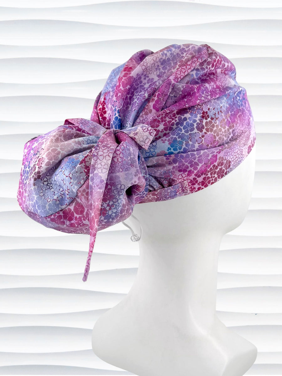 Euro Pony style surgical scrub cap by JensCaps with small daisies in pink, blue, and purple all over cotton fabric and displayed on a mannequin head