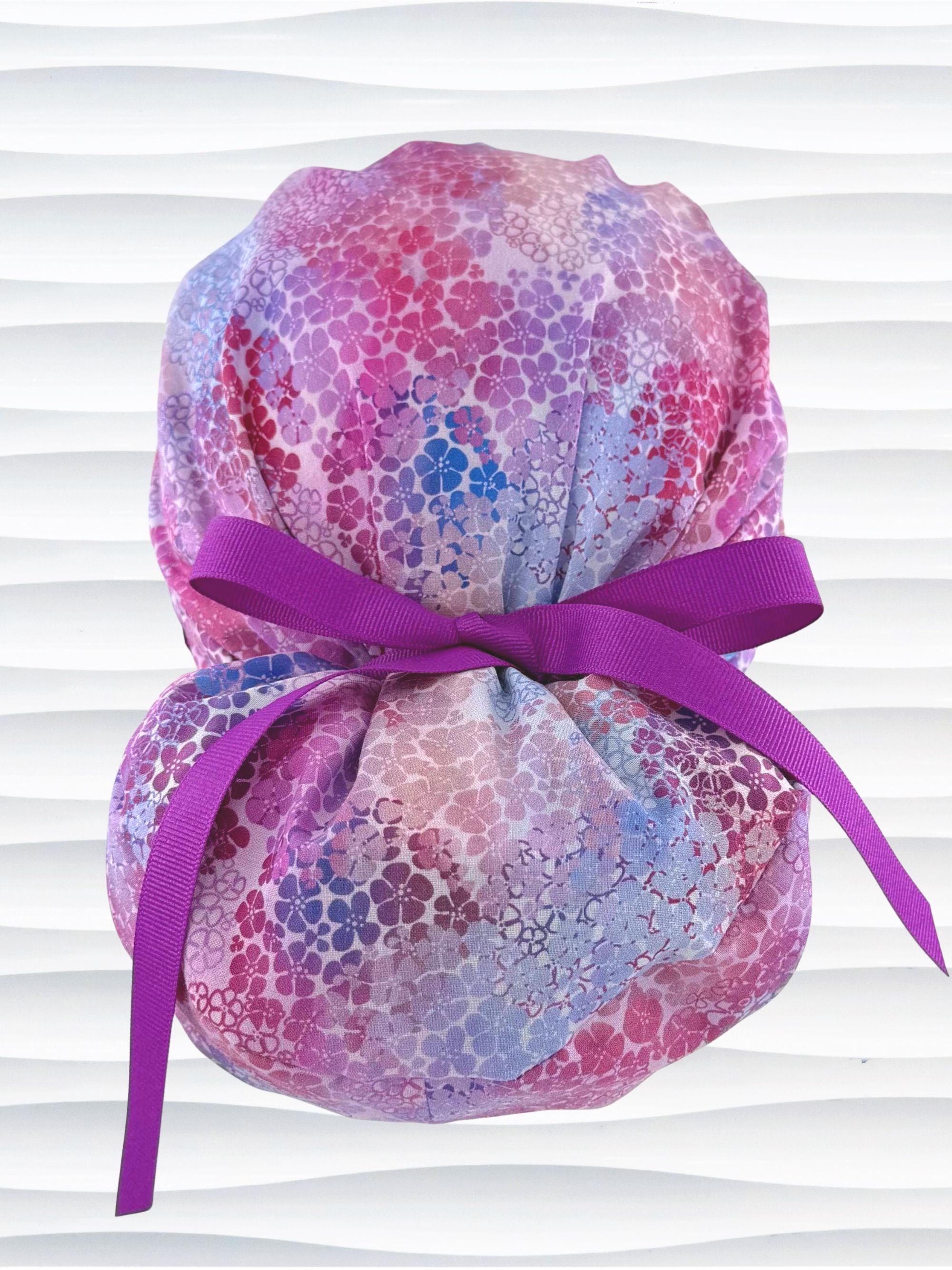 Euro Pony style surgical scrub cap by JensCaps with small daisies in pink, blue, and purple all over cotton fabric and displayed on a mannequin head