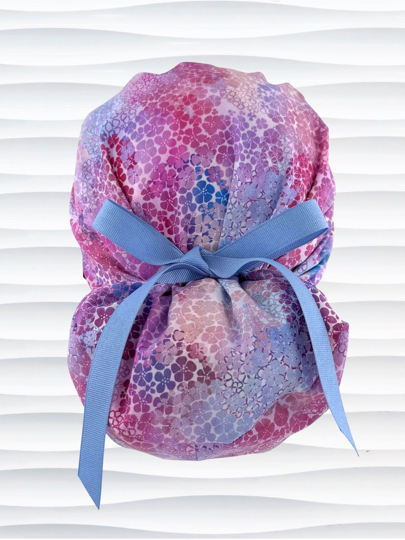 Euro Pony style surgical scrub cap by JensCaps with small daisies in pink, blue, and purple all over cotton fabric and displayed on a mannequin head