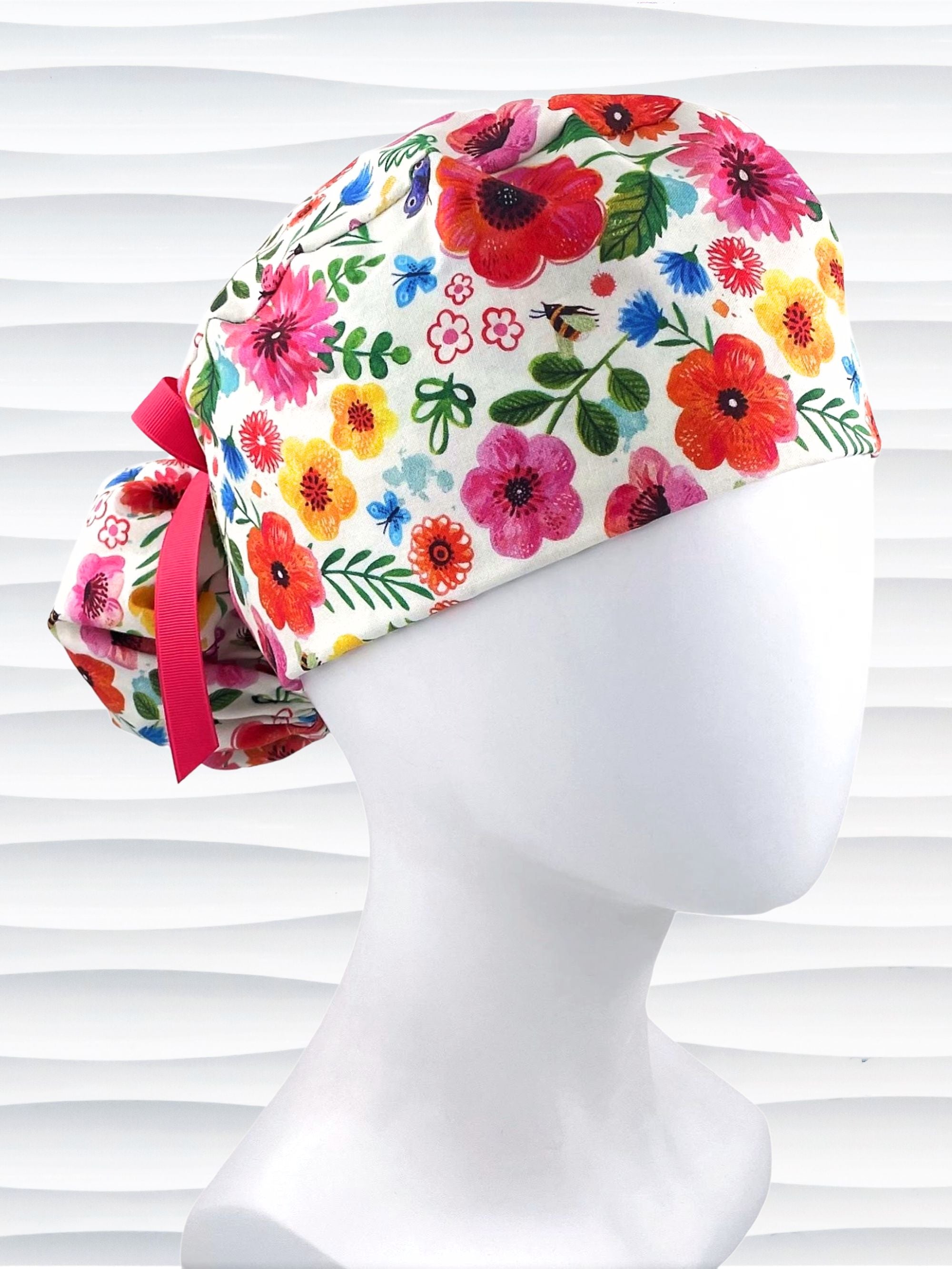 Ponytail style scrub cap hat with flowers and bees and butterflies on white premium cotton and tied with grosgrain ribbon.