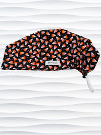 A Pixie style black scrub cap by JensCaps with an orange, white, and pink candy corn pattern, displayed on a white mannequin head