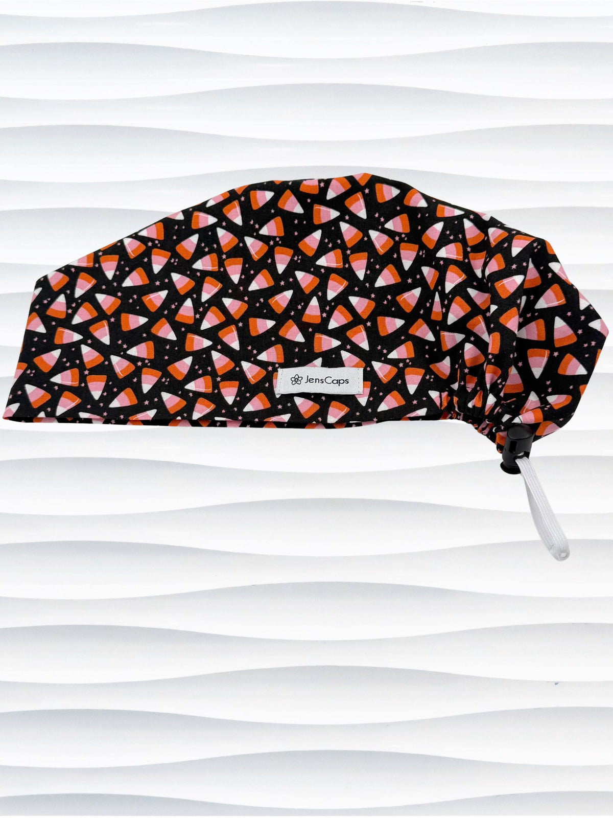 A Pixie style black scrub cap by JensCaps with an orange, white, and pink candy corn pattern, displayed on a white mannequin head