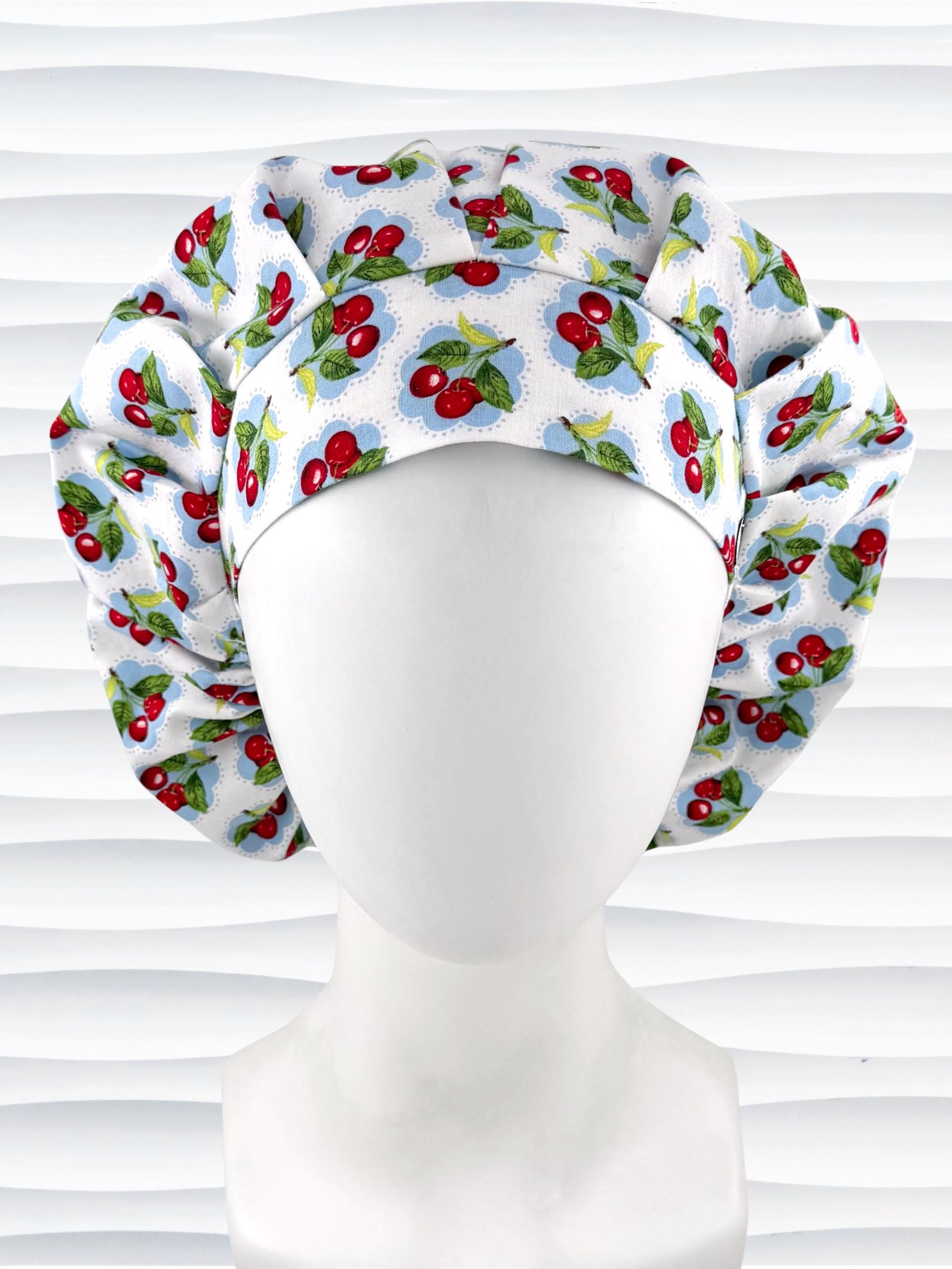 Bouffant style surgical scrub cap by JensCaps with red cherries and blue polka dots on white cotton fabric and displayed on a mannequin head.