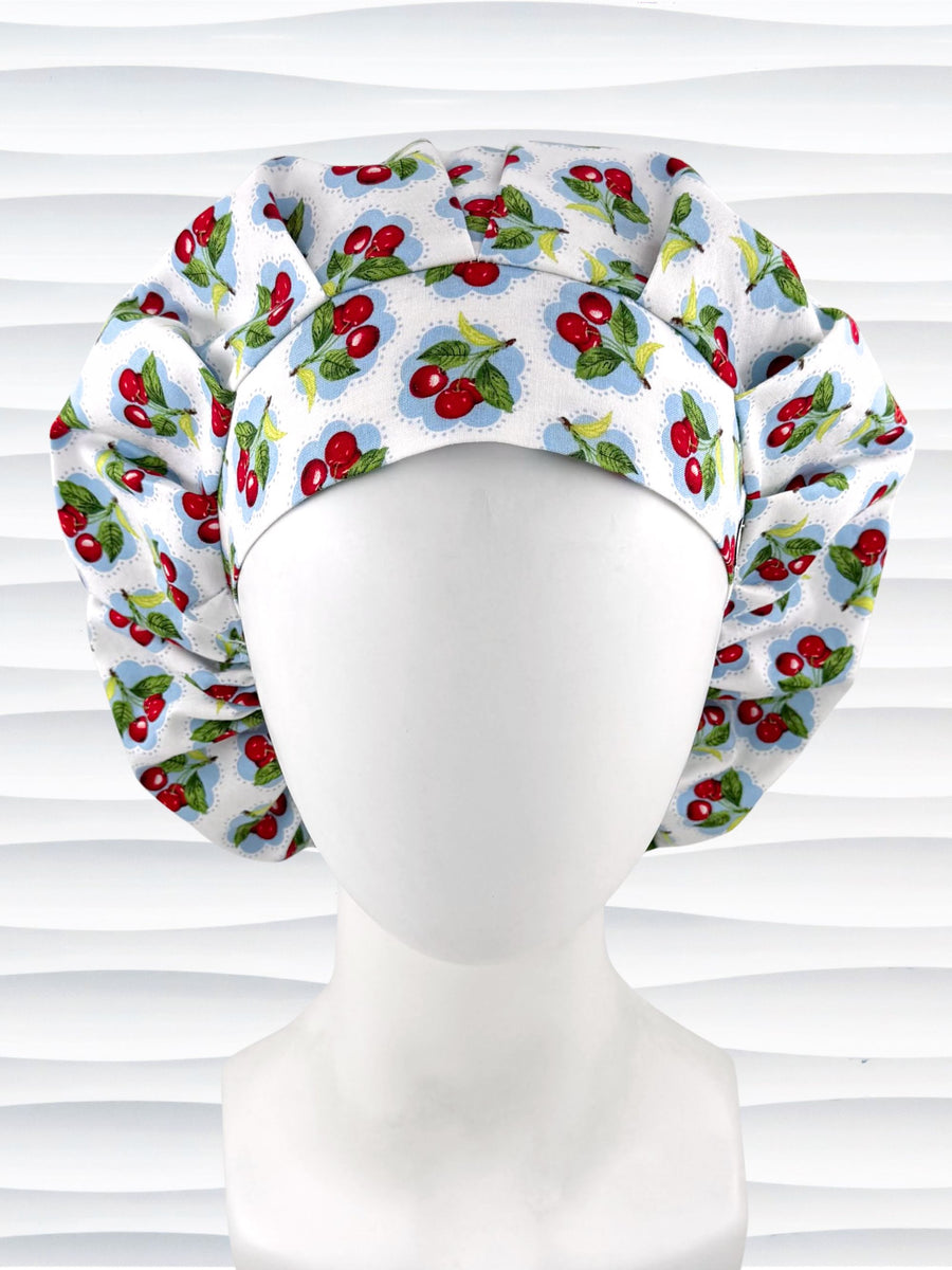 Bouffant style surgical scrub cap by JensCaps with red cherries and blue polka dots on white cotton fabric and displayed on a mannequin head.