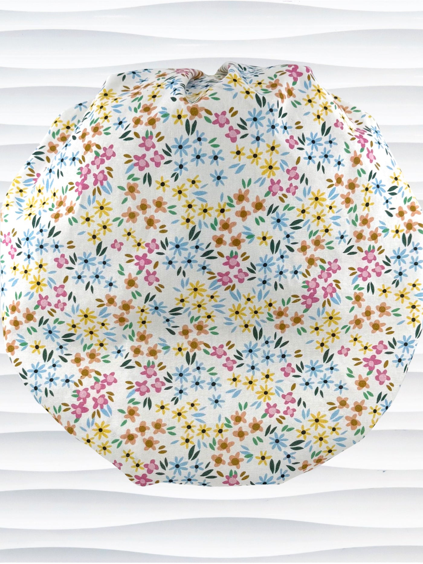 A white fabric bouffant style surgical cap by JensCaps with a colorful floral print, displayed on a white mannequin head against a white wavy background.