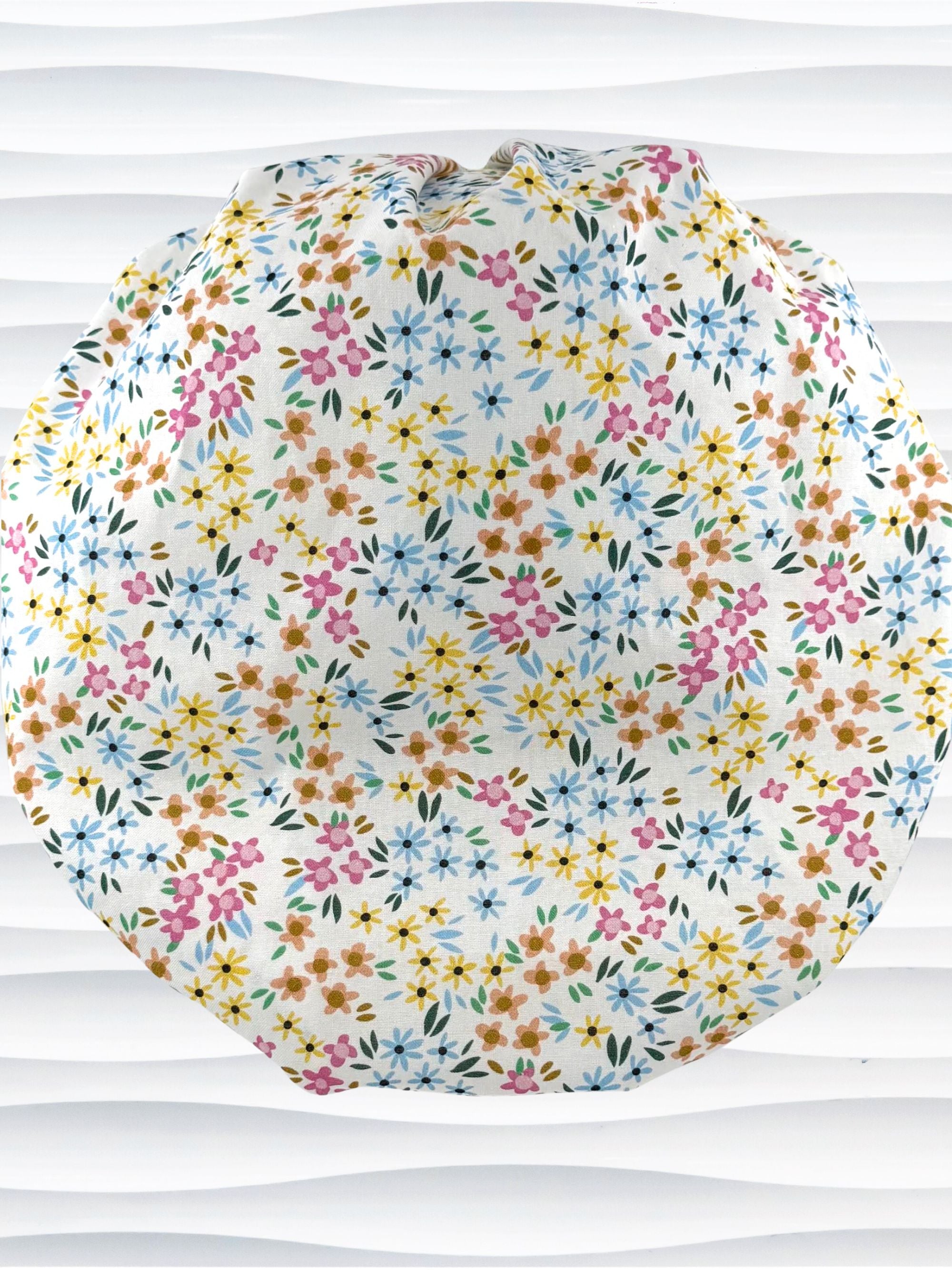 A white fabric bouffant style surgical cap by JensCaps with a colorful floral print, displayed on a white mannequin head against a white wavy background.