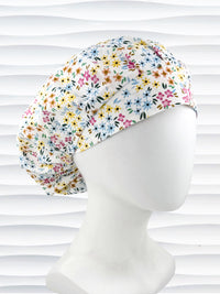 A white fabric bouffant style surgical cap by JensCaps with a colorful floral print, displayed on a white mannequin head against a white wavy background.