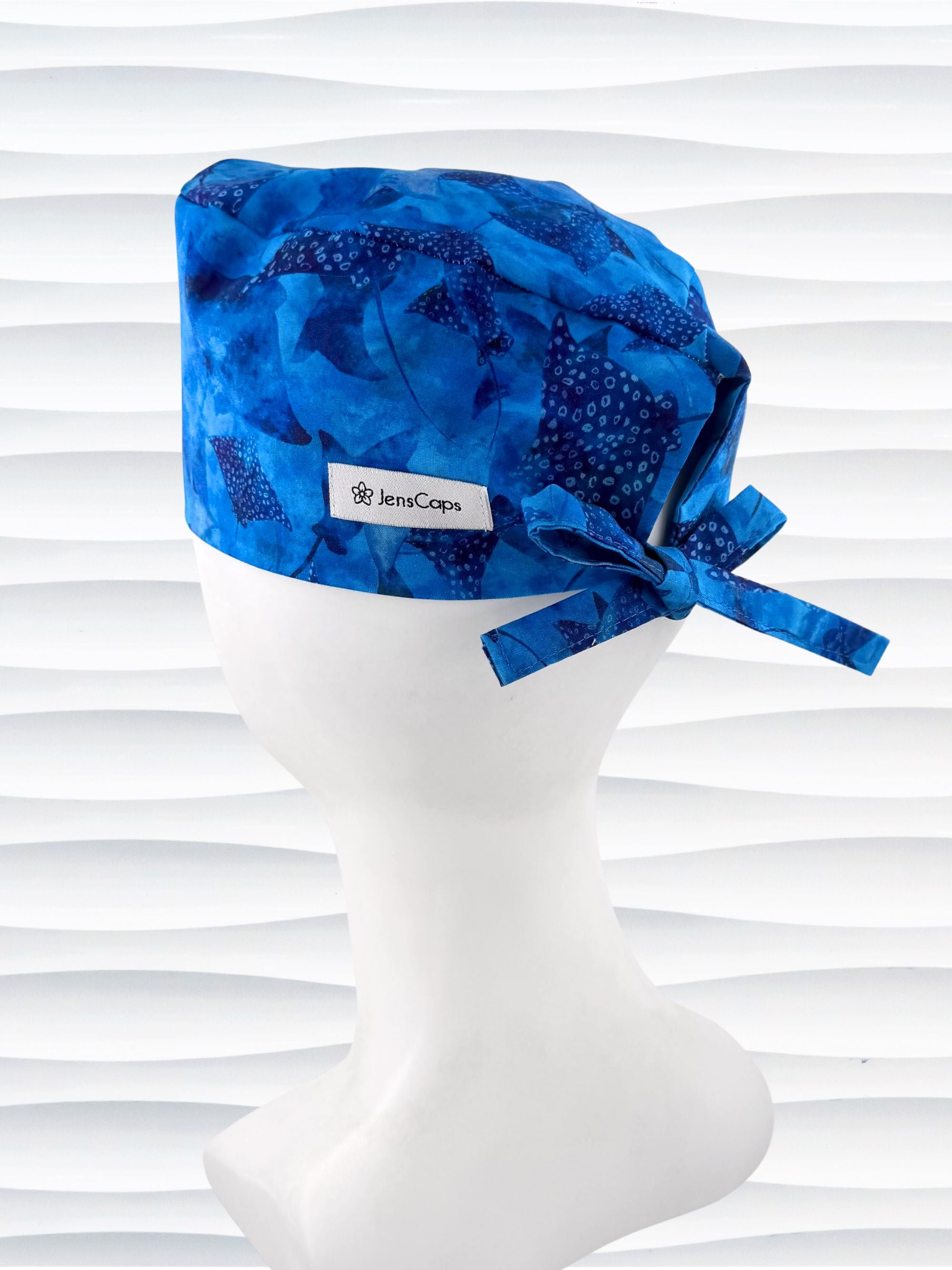 Tie back surgeon style scrub cap by JensCaps with blue fish and ocean stingrays on cotton fabric and displayed on a white mannequin head.