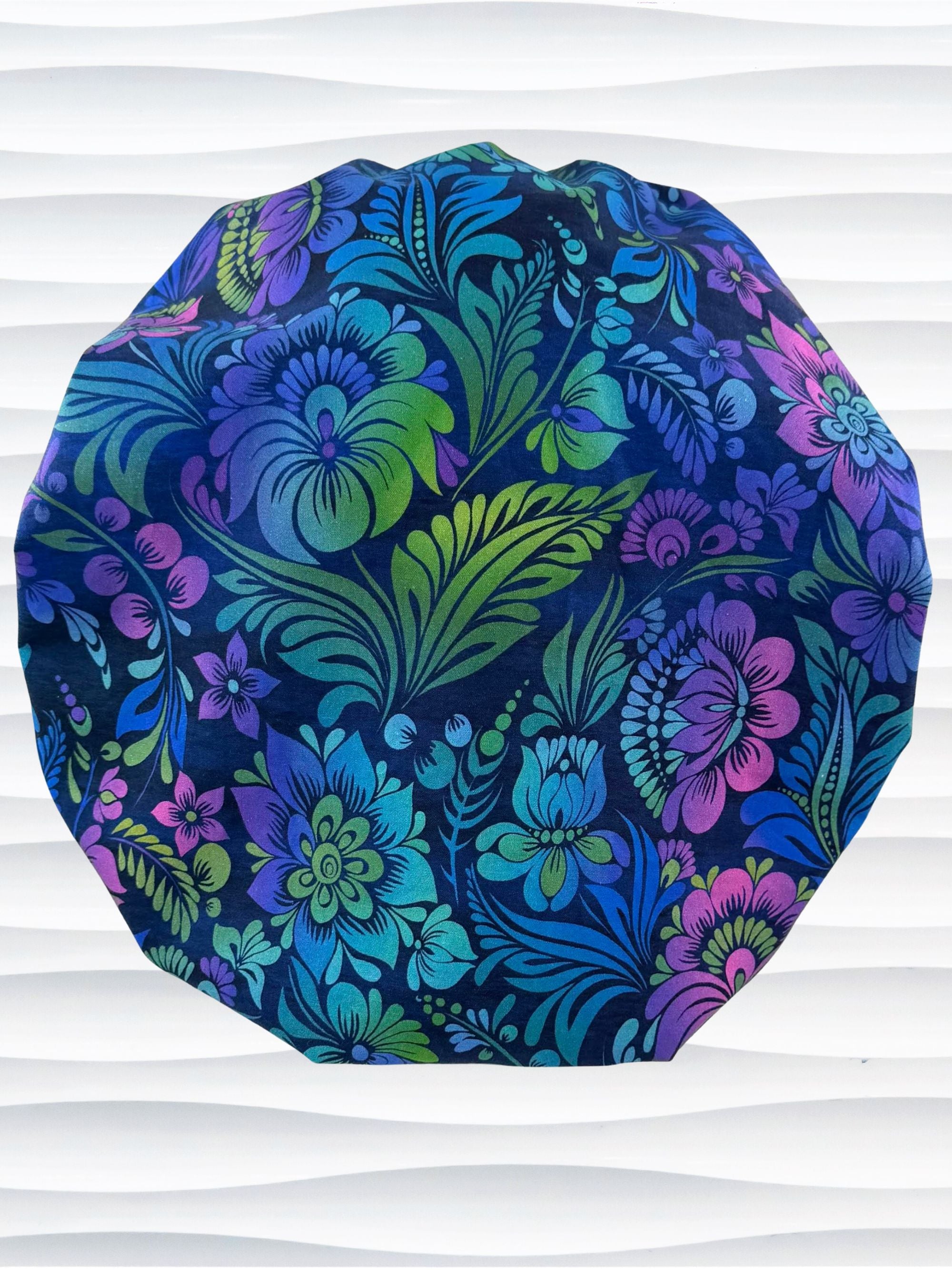 Bouffant style surgical scrub cap by JensCaps with an allover floral pattern in dark blue, purple, emerald, and turquoise and displayed on a mannequin head.