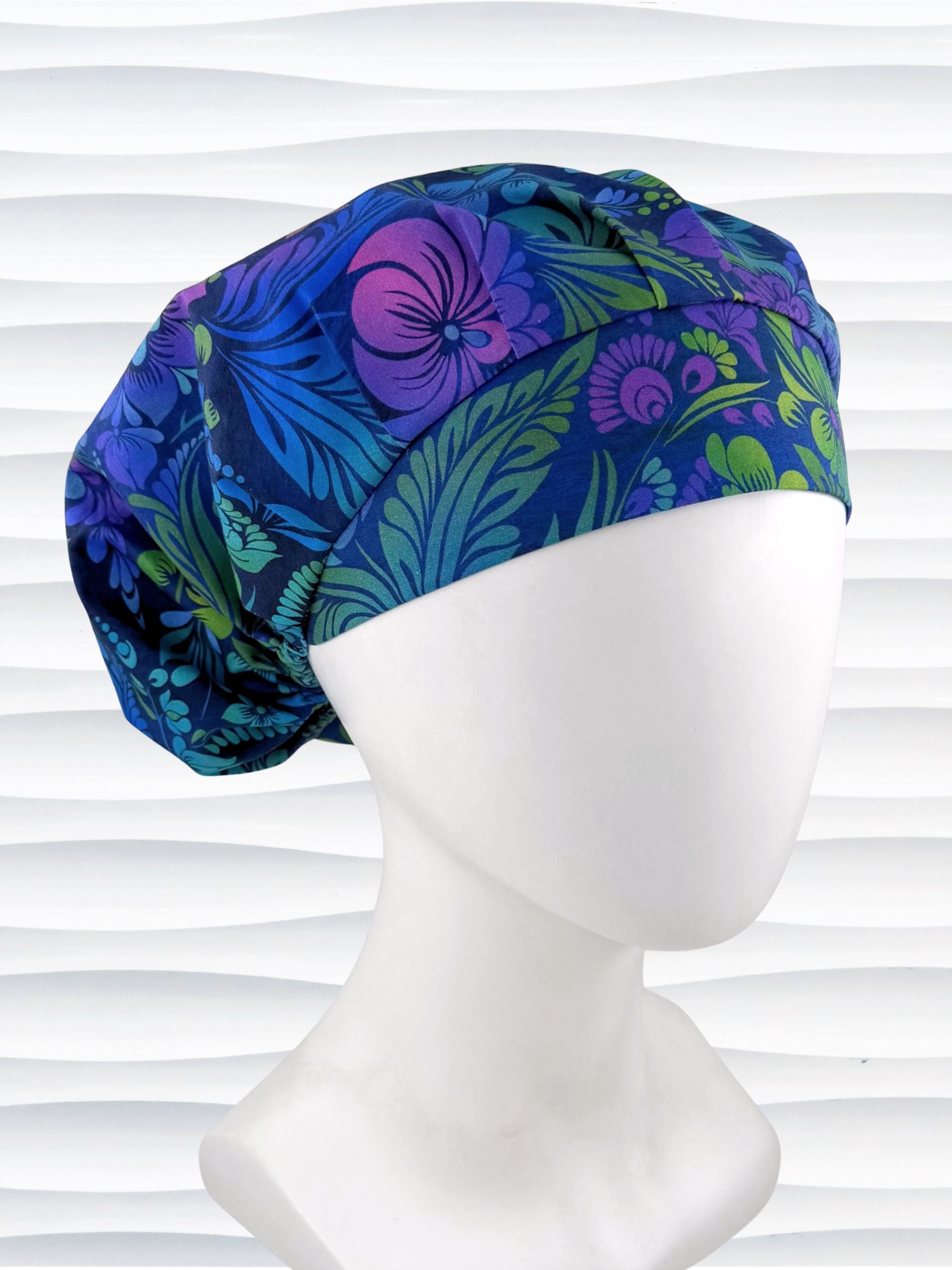 Bouffant style surgical scrub cap by JensCaps with an allover floral pattern in dark blue, purple, emerald, and turquoise and displayed on a mannequin head.
