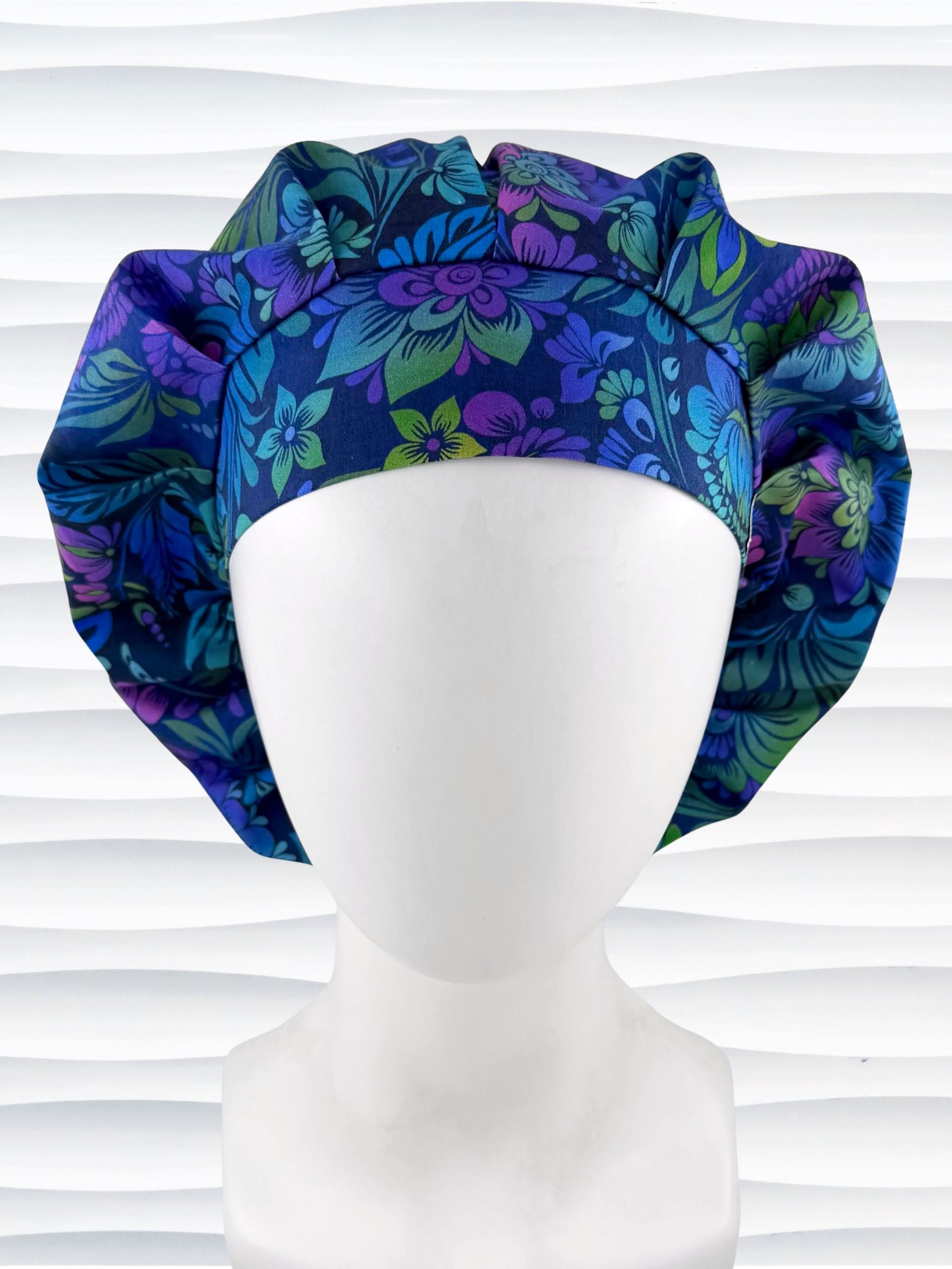 Bouffant style surgical scrub cap by JensCaps with an allover floral pattern in dark blue, purple, emerald, and turquoise and displayed on a mannequin head.