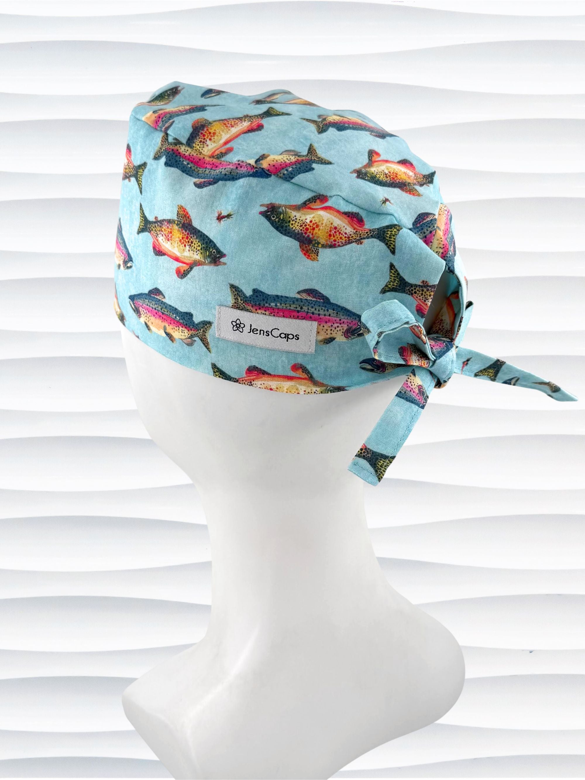 Tie back style surgical scrub cap by JensCaps with colorful fish on a light blue fabric and displayed on a white mannequin head