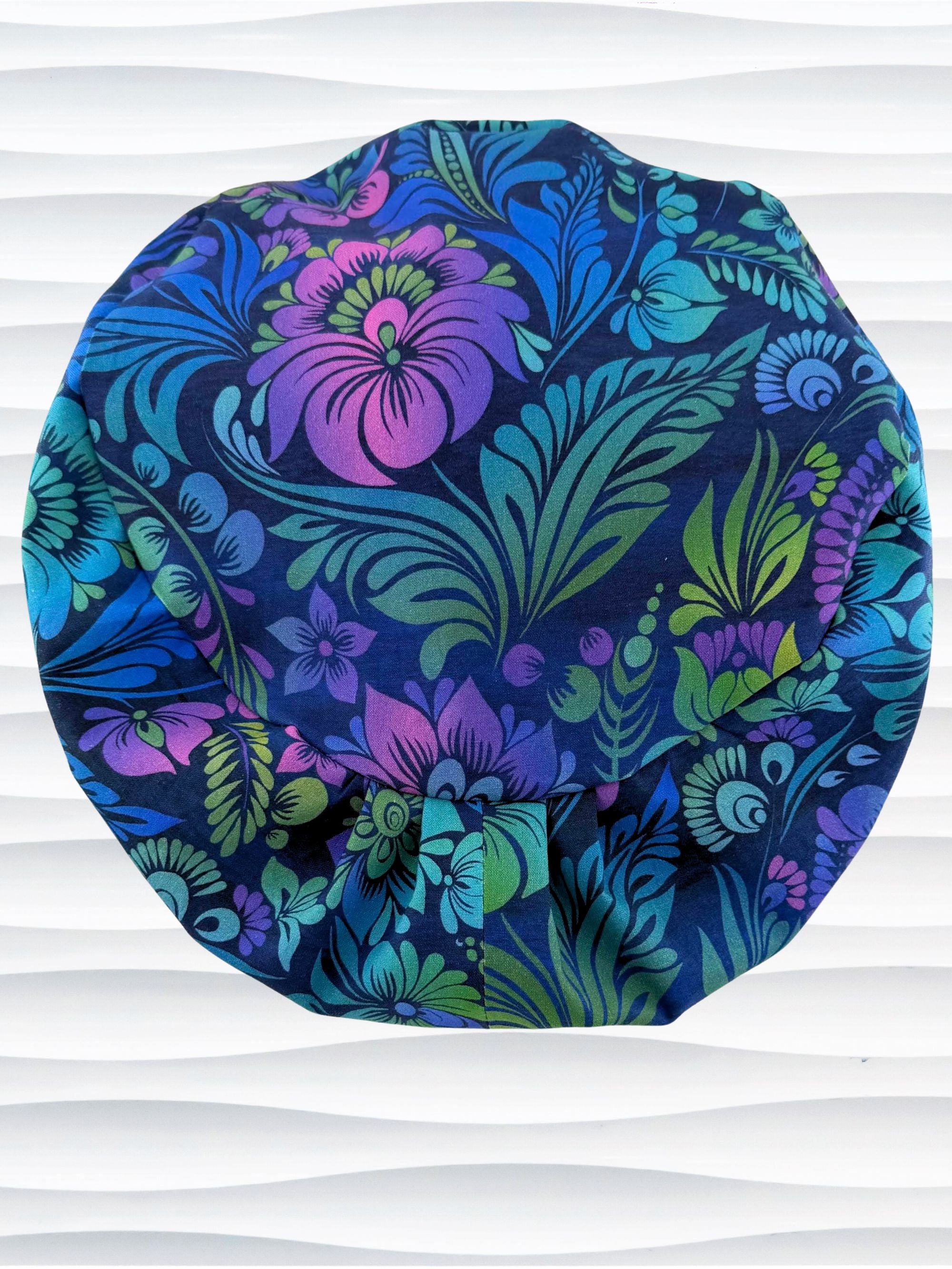 Euro Pixie style surgical scrub cap by JensCaps with an allover floral pattern in dark blue, purple, emerald, and turquoise and displayed on a mannequin head.
