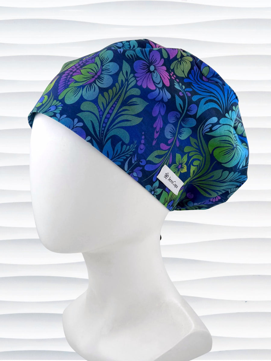 Euro Pixie style surgical scrub cap by JensCaps with an allover floral pattern in dark blue, purple, emerald, and turquoise and displayed on a mannequin head.