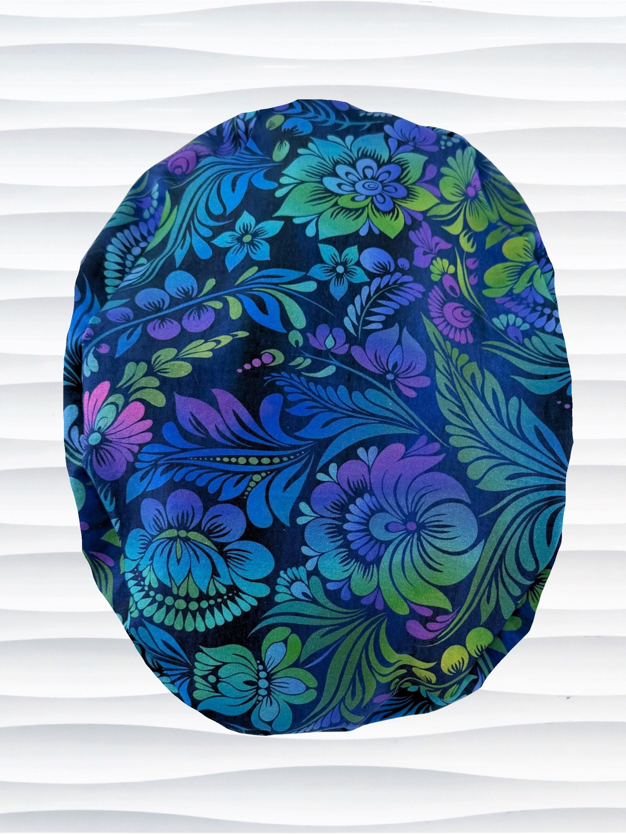 Euro Pony style surgical scrub cap by JensCaps with an allover floral pattern in dark blue, purple, emerald, and turquoise and displayed on a mannequin head.