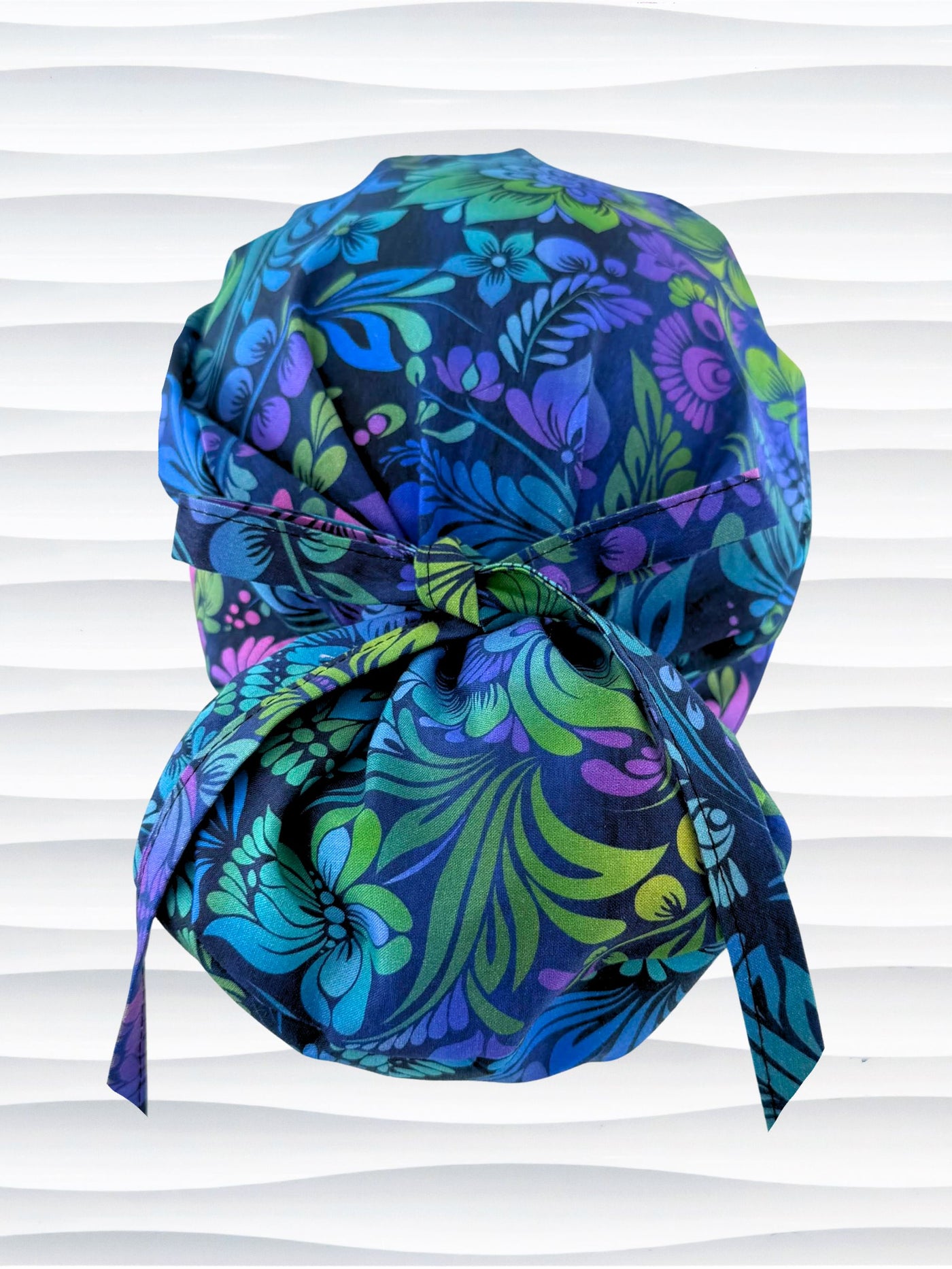 Euro Pony style surgical scrub cap by JensCaps with an allover floral pattern in dark blue, purple, emerald, and turquoise and displayed on a mannequin head.