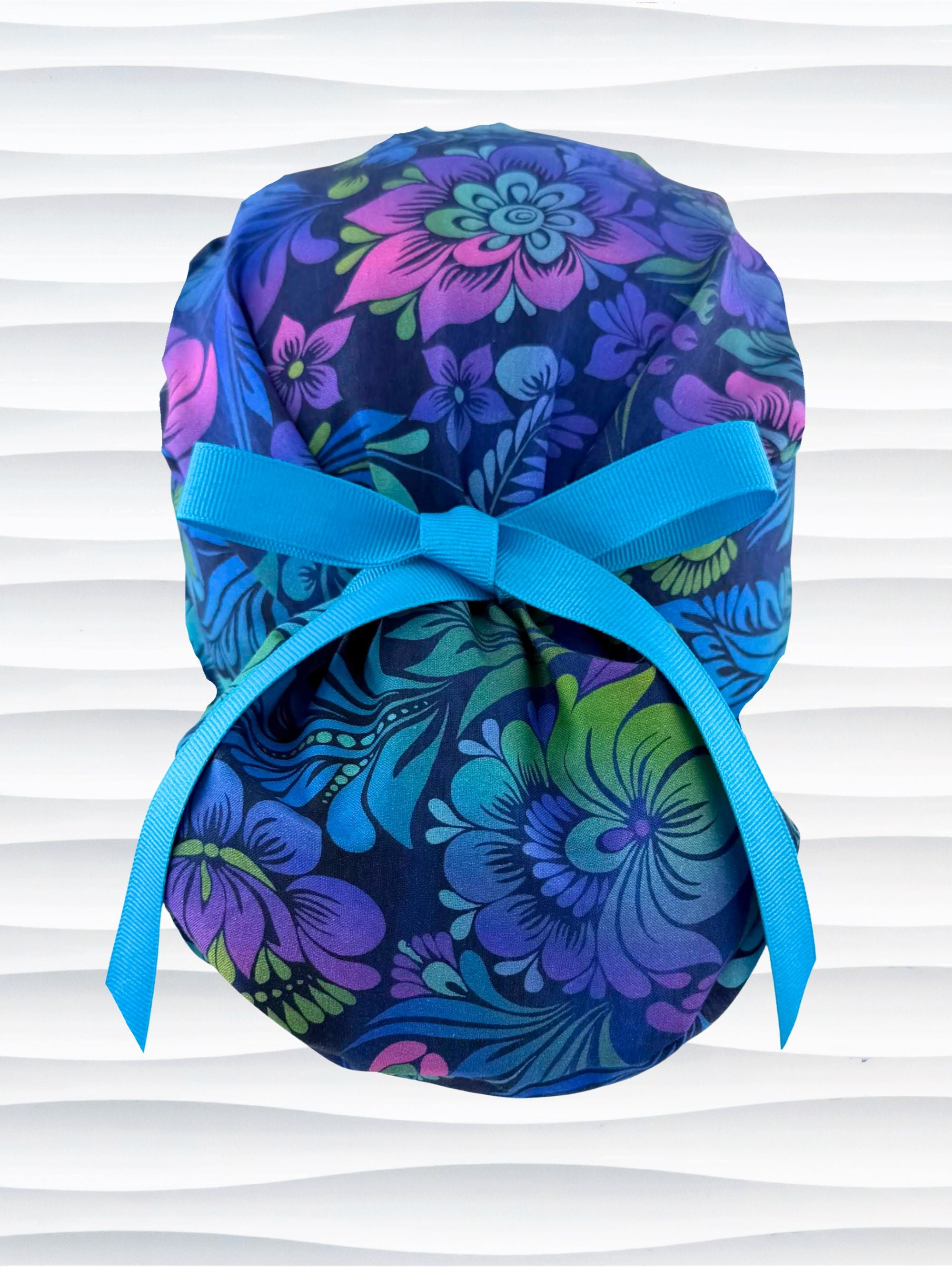 Euro Pony style surgical scrub cap by JensCaps with an allover floral pattern in dark blue, purple, emerald, and turquoise and displayed on a mannequin head.