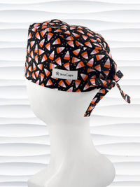 A black tie back style surgical scrub cap with a pink, orange, and white candy corn pattern displayed on a white mannequin head. The brand name 'JensCaps' is visible on a white label sewn onto the side of the cap.