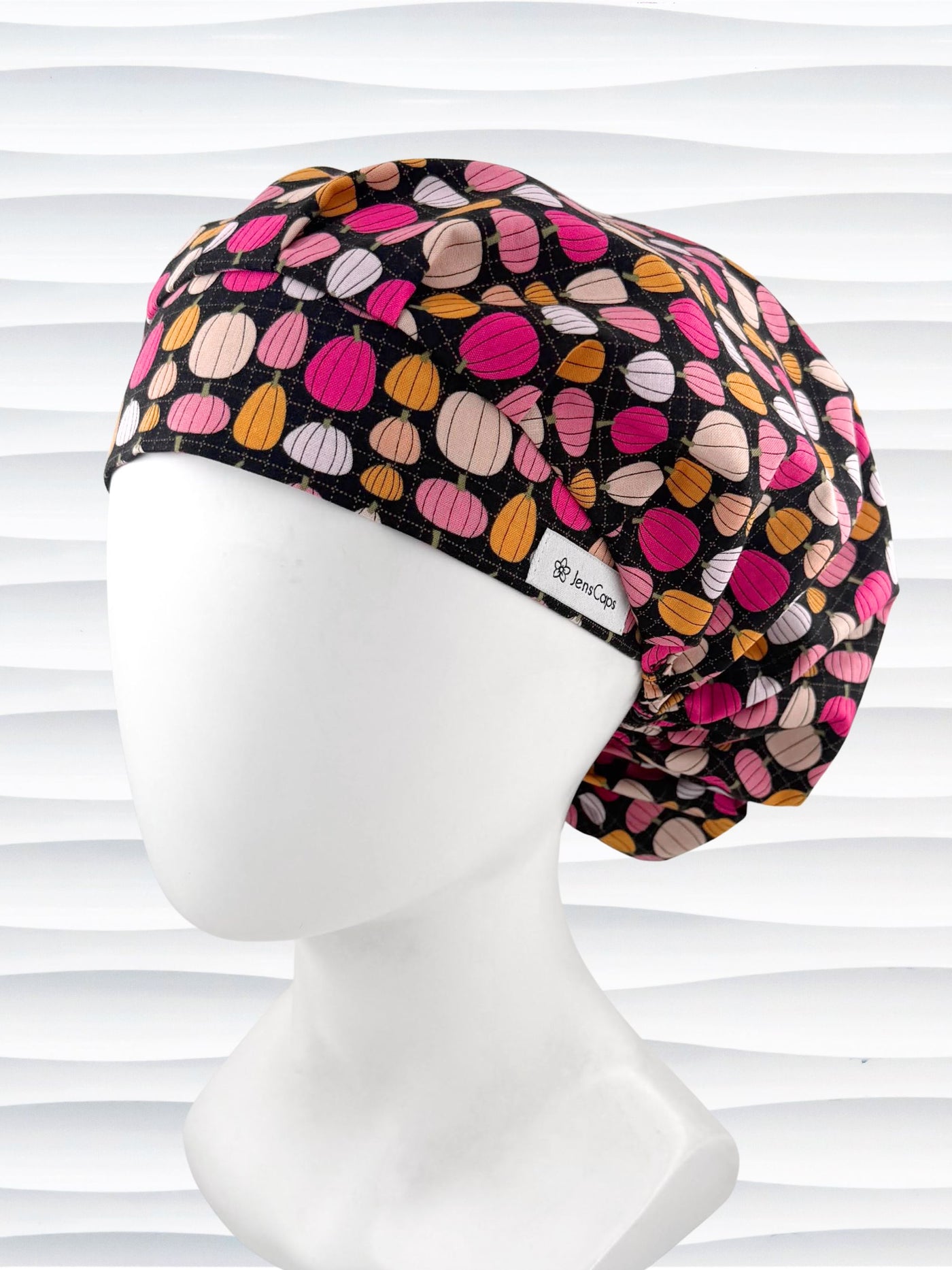 Bouffant style surgical scrub cap by JensCaps with pink and orange pumpkins on black cotton fabric and displayed on a mannequin head.