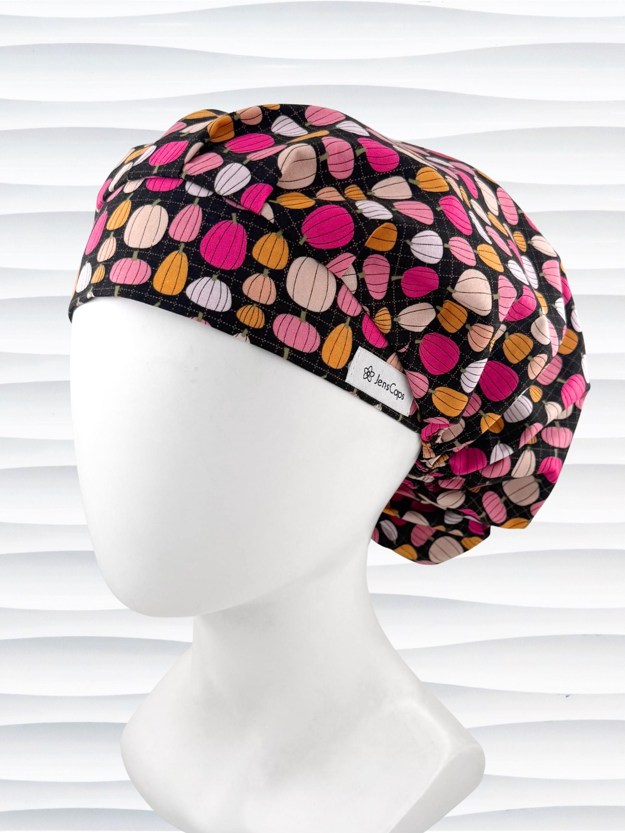 Bouffant style surgical scrub cap by JensCaps with pink and orange pumpkins on black cotton fabric and displayed on a mannequin head.