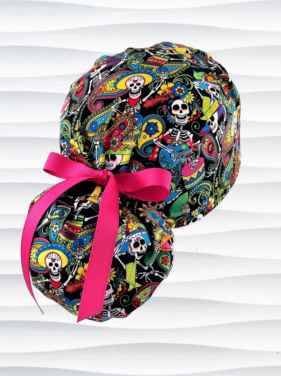 Ponytail scrub cap hat with day of the dead in bright colors on black cotton fabric and finished with grosgrain ribbon ties.