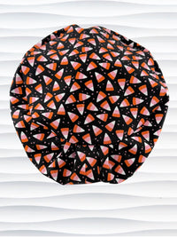 A Pixie style black scrub cap by JensCaps with an orange, white, and pink candy corn pattern, displayed on a white mannequin head