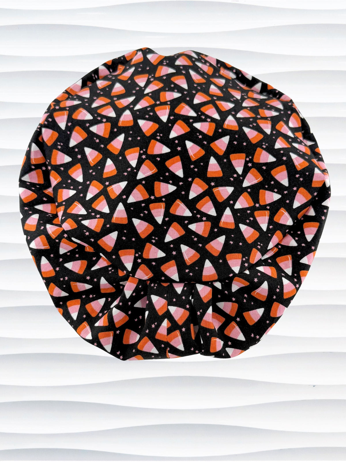 A Pixie style black scrub cap by JensCaps with an orange, white, and pink candy corn pattern, displayed on a white mannequin head