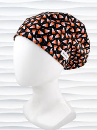 A Pixie style black scrub cap by JensCaps with an orange, white, and pink candy corn pattern, displayed on a white mannequin head