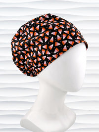 A Pixie style black scrub cap by JensCaps with an orange, white, and pink candy corn pattern, displayed on a white mannequin head