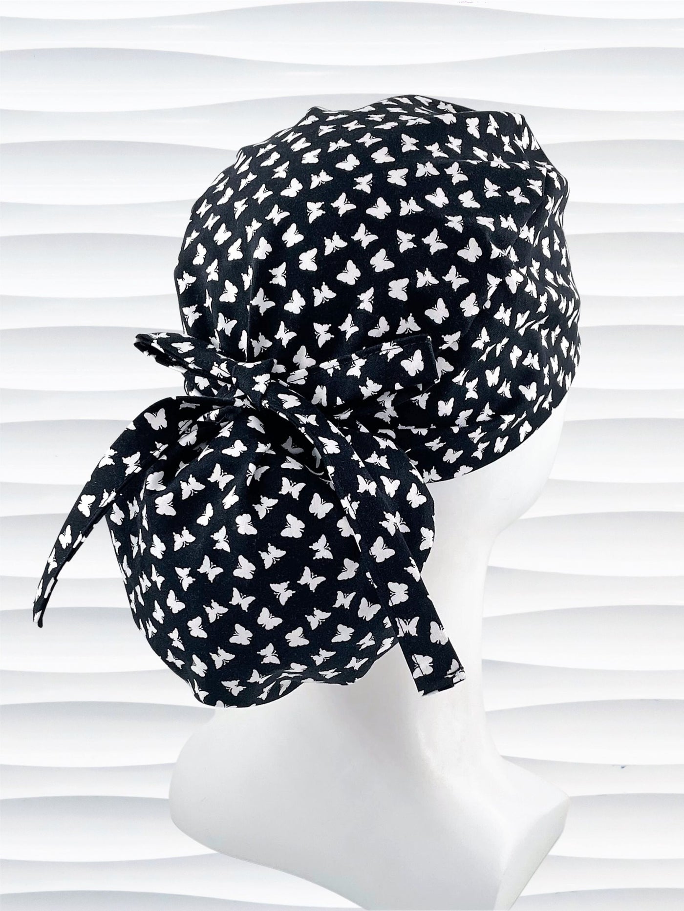 Ponytail style scrub cap hat with white butterflies on black cotton fabric.