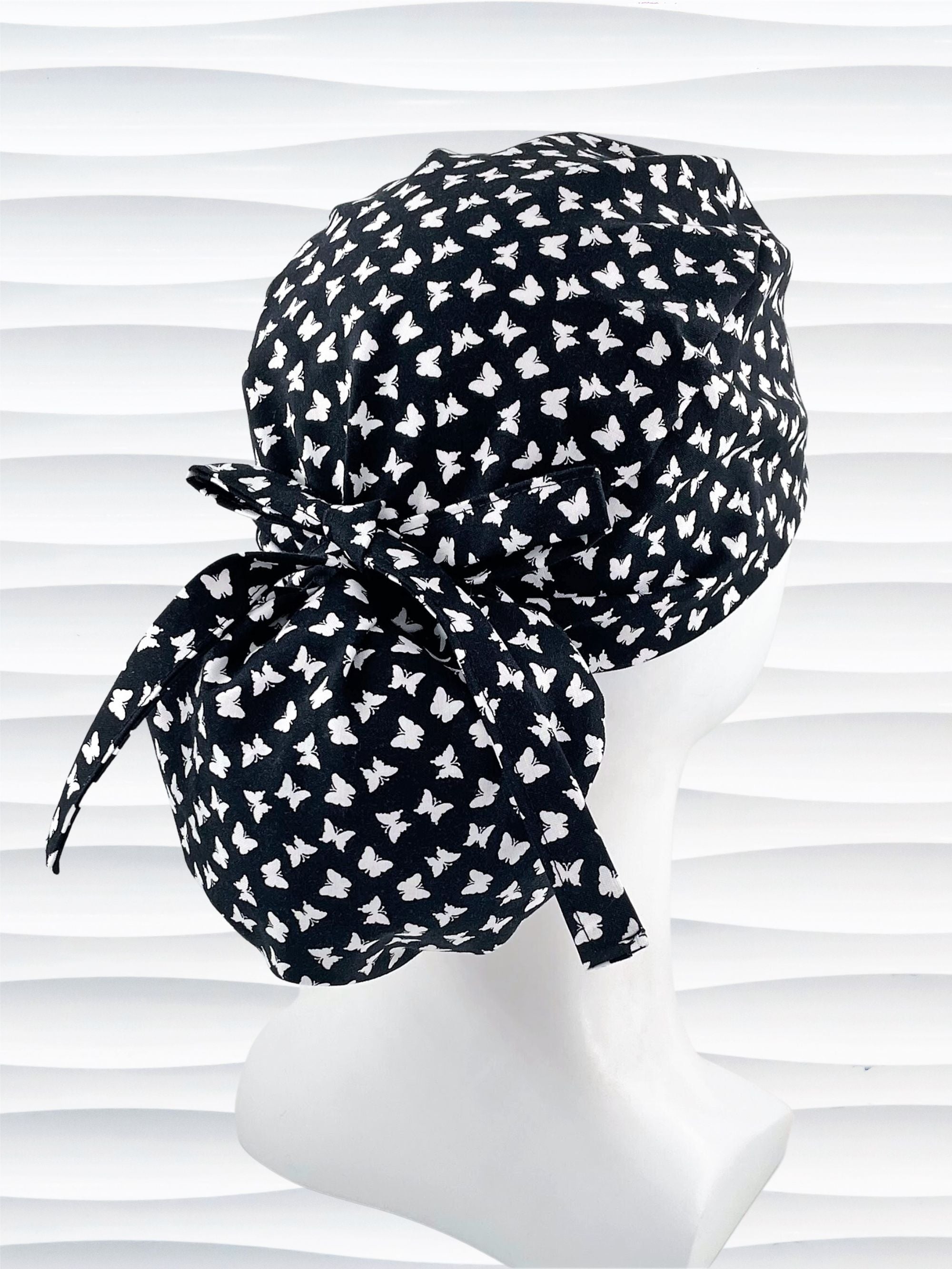Ponytail style scrub cap hat with white butterflies on black cotton fabric.