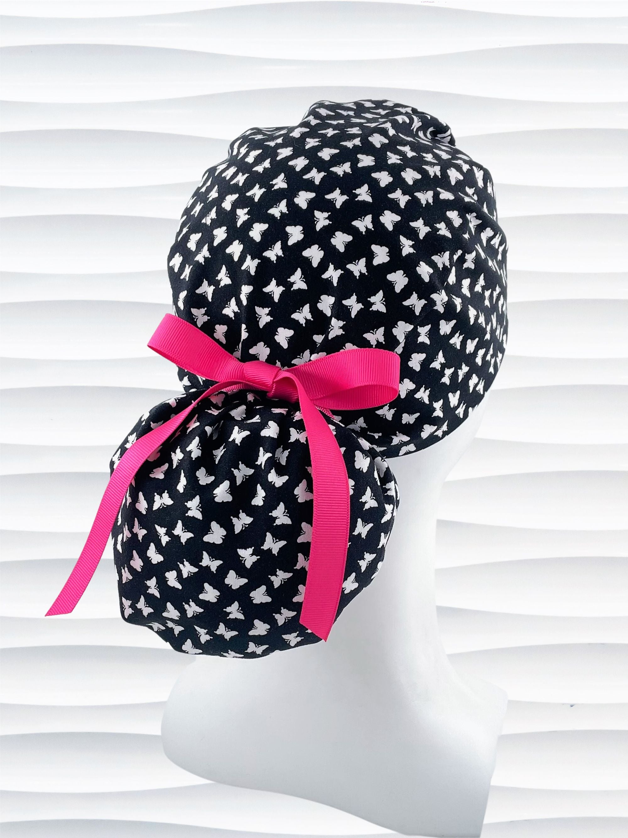 Ponytail style scrub cap hat with white butterflies on black cotton fabric.