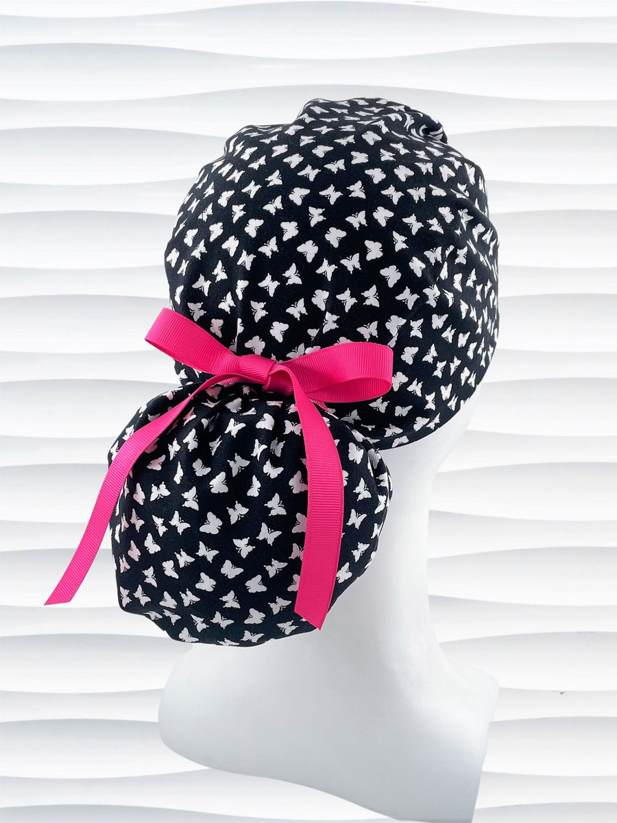 Ponytail style scrub cap hat with white butterflies on black cotton fabric.