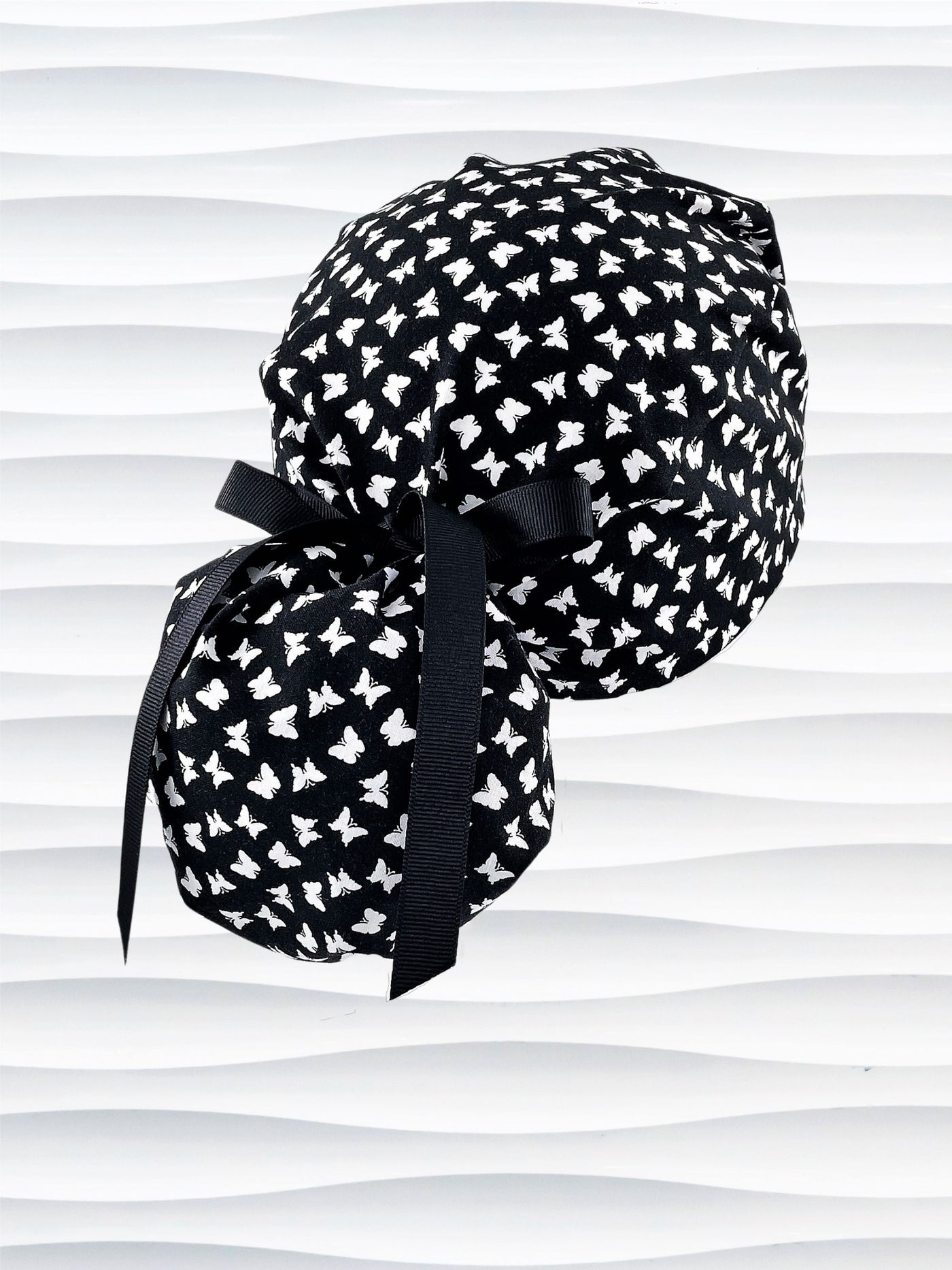 Ponytail style scrub cap hat with white butterflies on black cotton fabric.