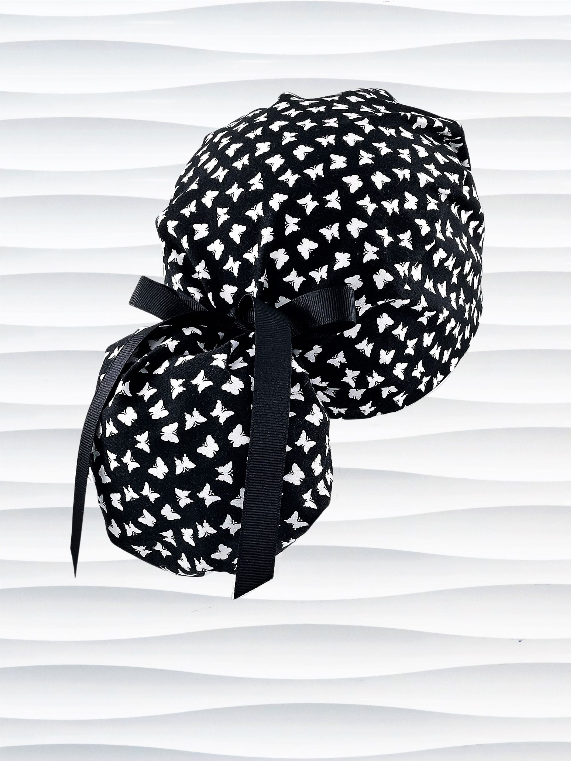 Ponytail style scrub cap hat with white butterflies on black cotton fabric.