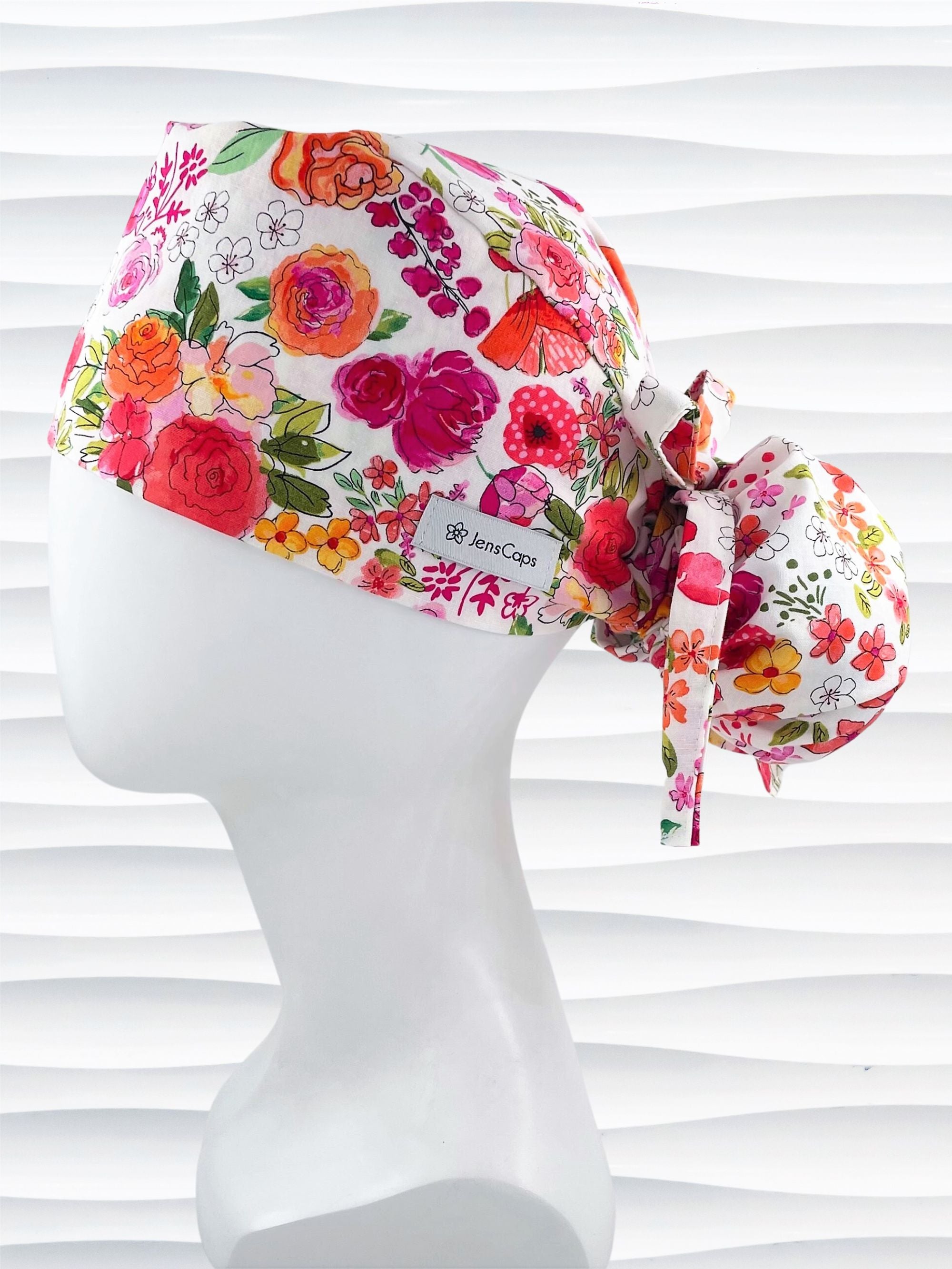 Ponytail style scrub cap with bright flowers on white cotton fabric and grosgrain ribbon ties
