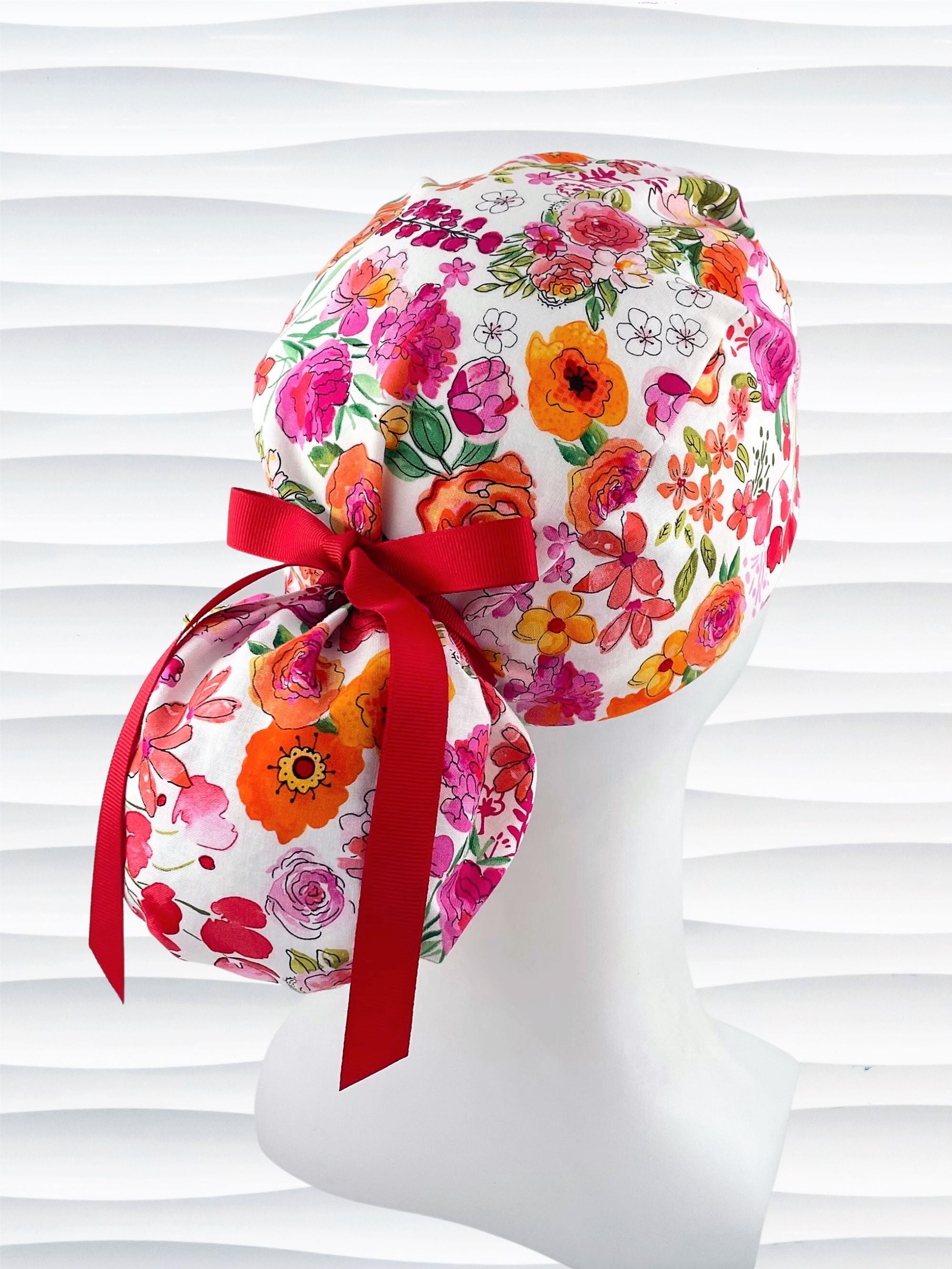 Ponytail style scrub cap with bright flowers on white cotton fabric and grosgrain ribbon ties