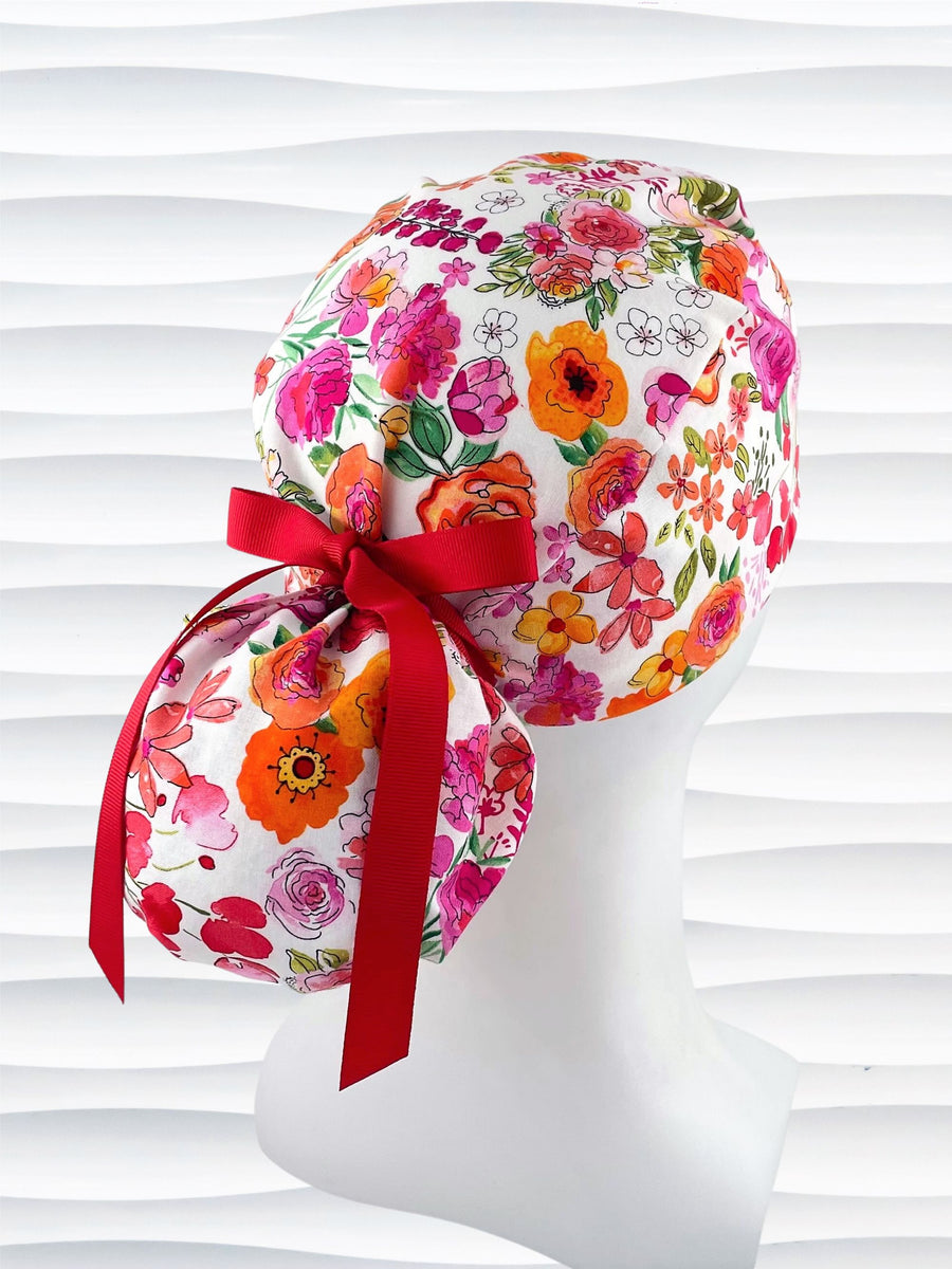 Ponytail style scrub cap with bright flowers on white cotton fabric and grosgrain ribbon ties