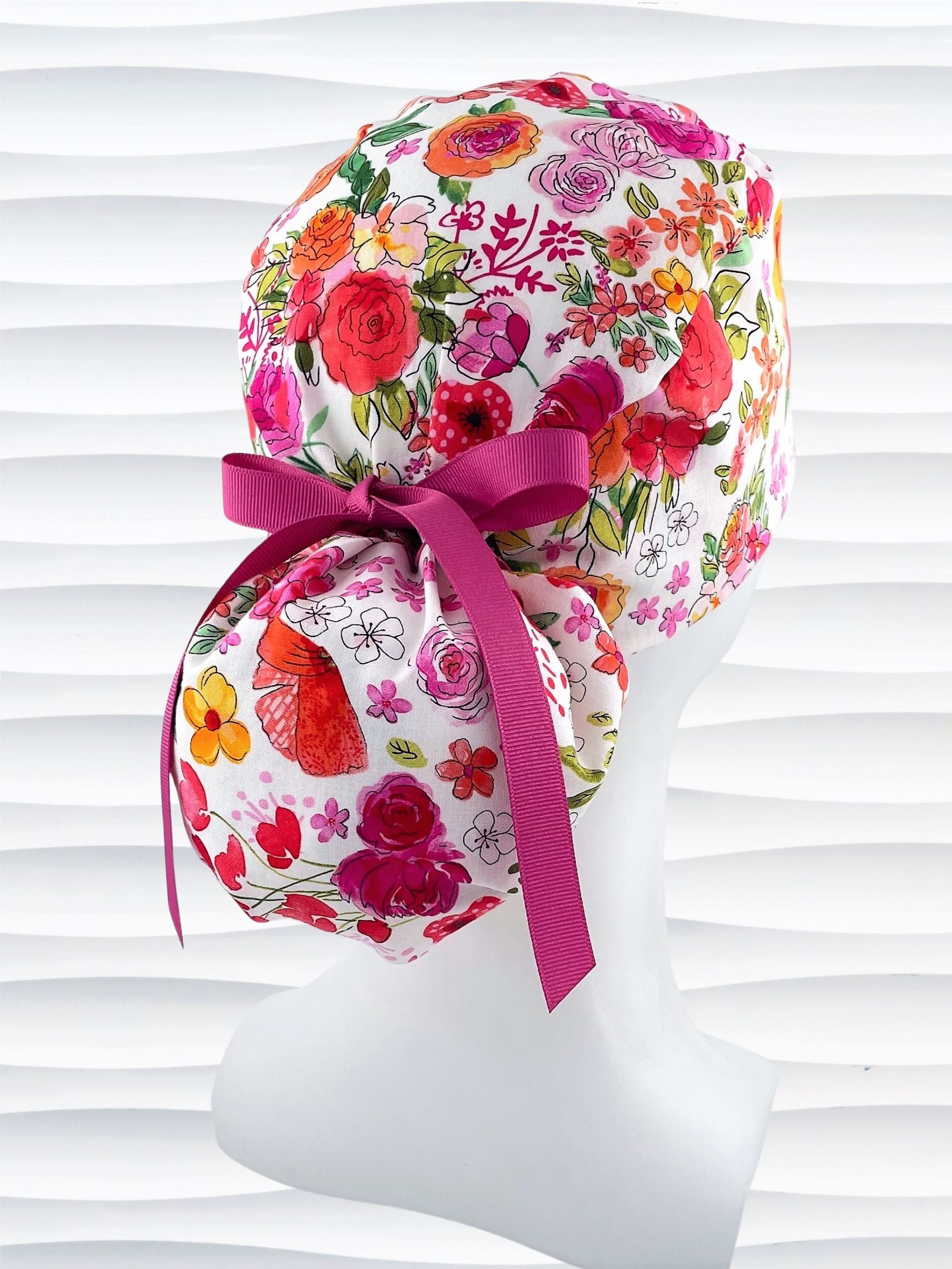 Ponytail style scrub cap with bright flowers on white cotton fabric and grosgrain ribbon ties