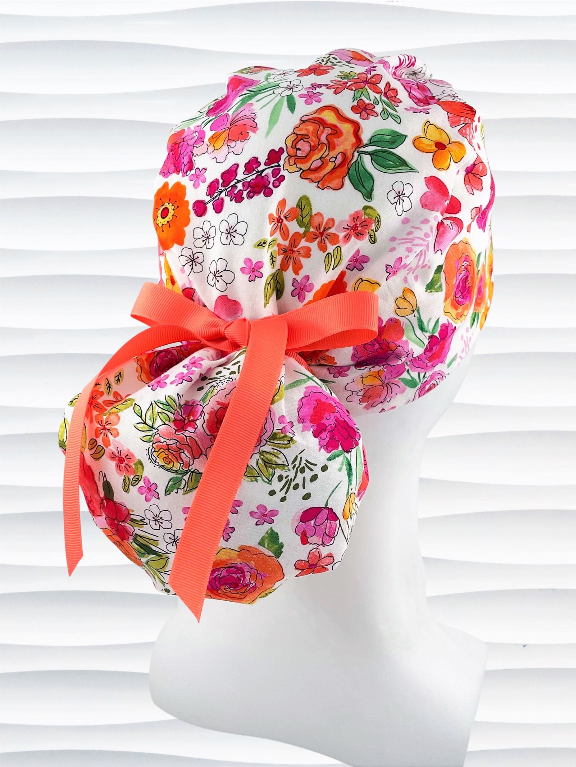 Ponytail style scrub cap with bright flowers on white cotton fabric and grosgrain ribbon ties