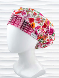 Bouffant style surgical scrub cap hat with pink, red, yellow, white, and orange flowers on white cotton fabric.