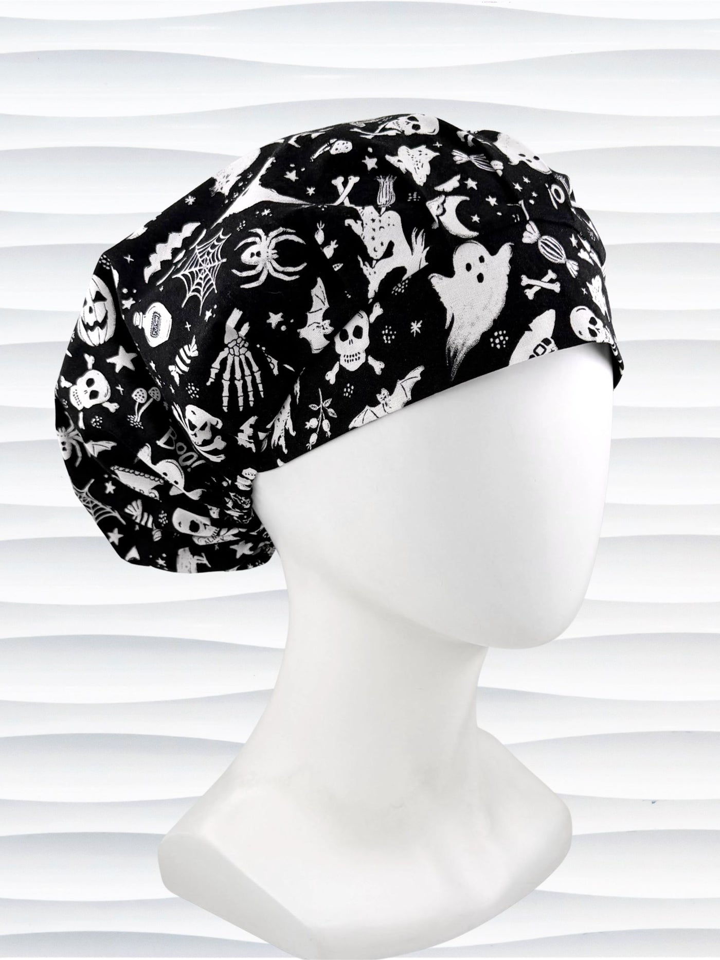 A black and white Halloween-themed Bouffant style surgical scrub cap by JensCaps with a printed pattern of ghosts, witches, pumpkins, and stars and displayed on a white mannequin head 