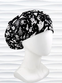 A black and white Halloween-themed Bouffant style surgical scrub cap by JensCaps with a printed pattern of ghosts, witches, pumpkins, and stars and displayed on a white mannequin head 